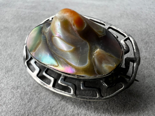 This vintage brooch showcases a tall abalone shell beautifully set within a sterling silver frame that features a classic Greek key design. Its elegant combination of natural iridescence and timeless pattern makes it a standout accessory that adds refined charm to any ensemble.