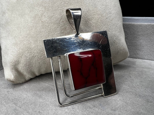 This striking sterling silver pendant features a bold blood red faux stone, designed to stand out beautifully with larger silver chains. Handcrafted in Mexico, it combines unique artistry with timeless elegance, making it a perfect statement piece to complement your collection.