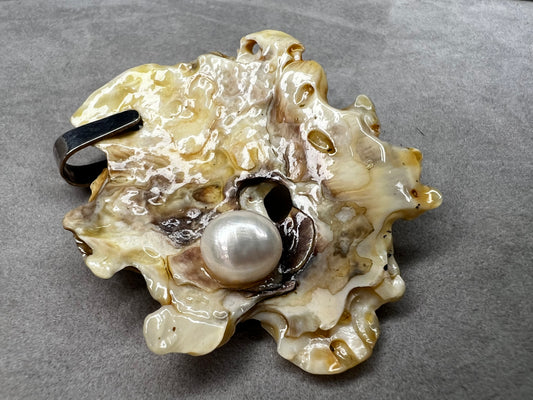 This pendant is crafted from a natural oyster and pearl, complemented by a sterling silver bail for a refined finish. Its unique design offers a special touch.