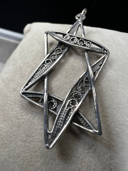 This sterling silver Star of David pendant, measuring nearly 2 inches, showcases intricate filigree craftsmanship. Its delicate design highlights expert artistry, making it a meaningful and elegant accessory.