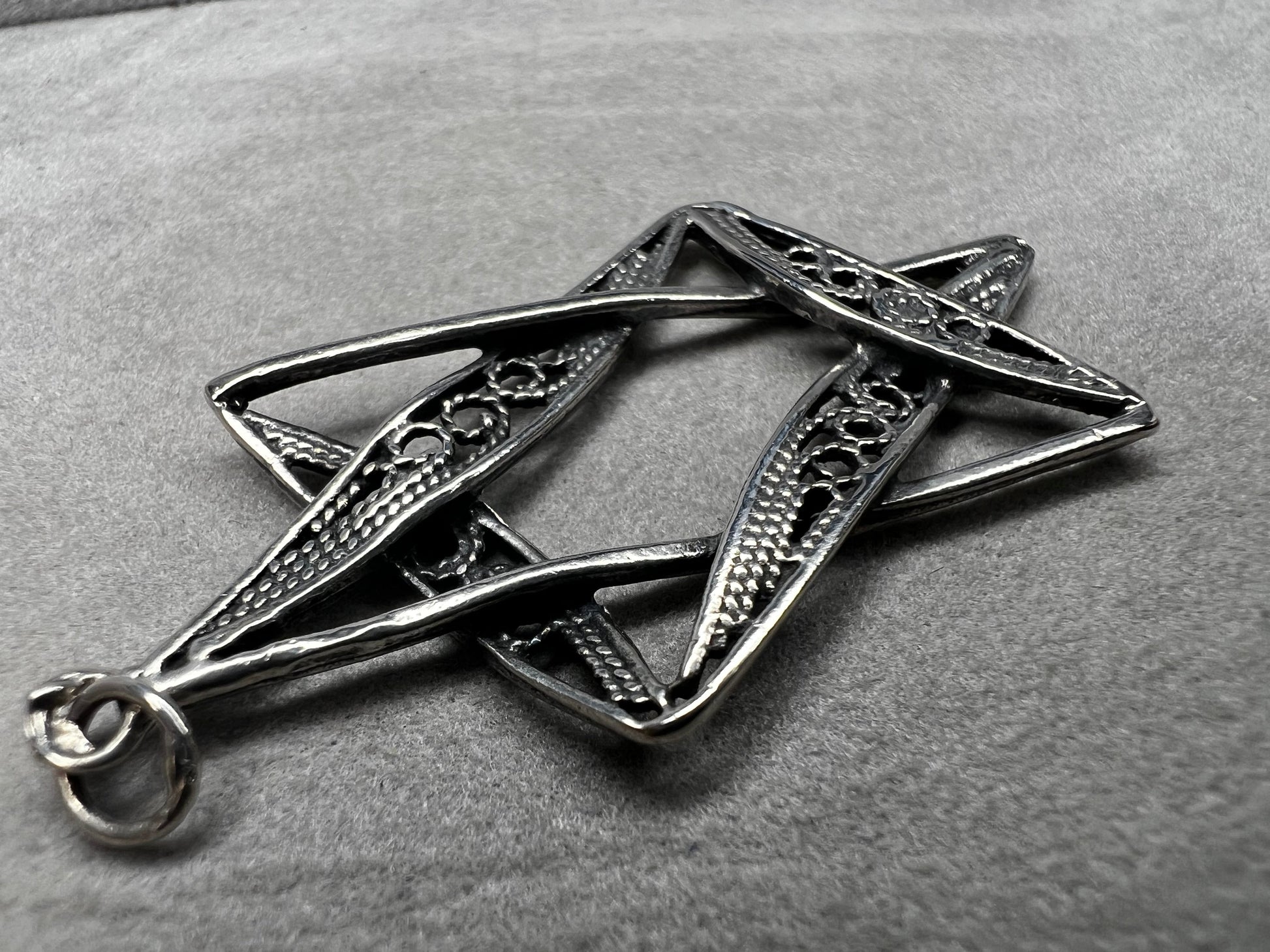 This sterling silver Star of David pendant, measuring nearly 2 inches, showcases intricate filigree craftsmanship. Its delicate design highlights expert artistry, making it a meaningful and elegant accessory.