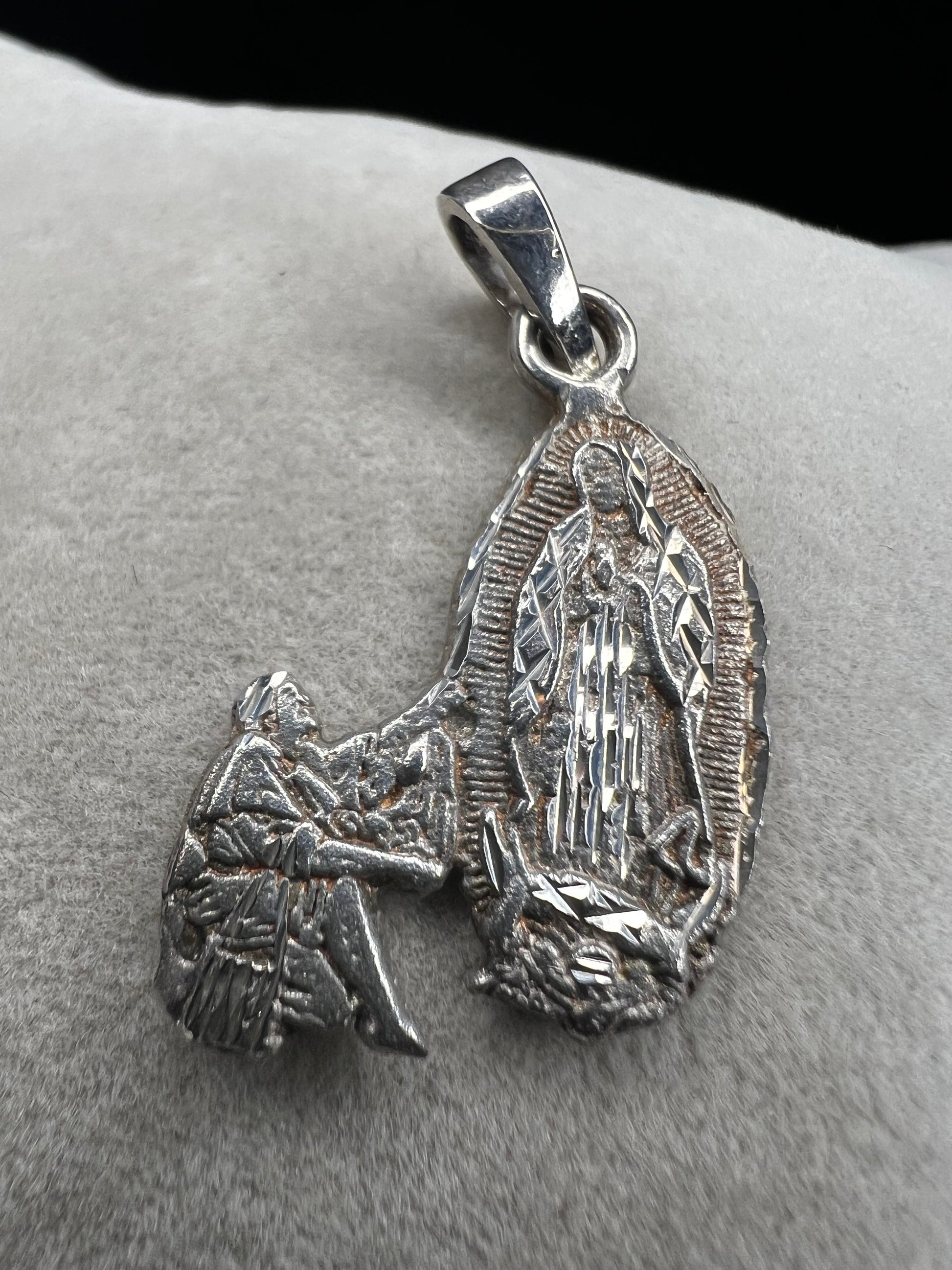 Crafted from sterling silver, this pendant shows a figure kneeling before another, suggestive of a religious deity. This piece is detailed with diamond cuts to catch the light.