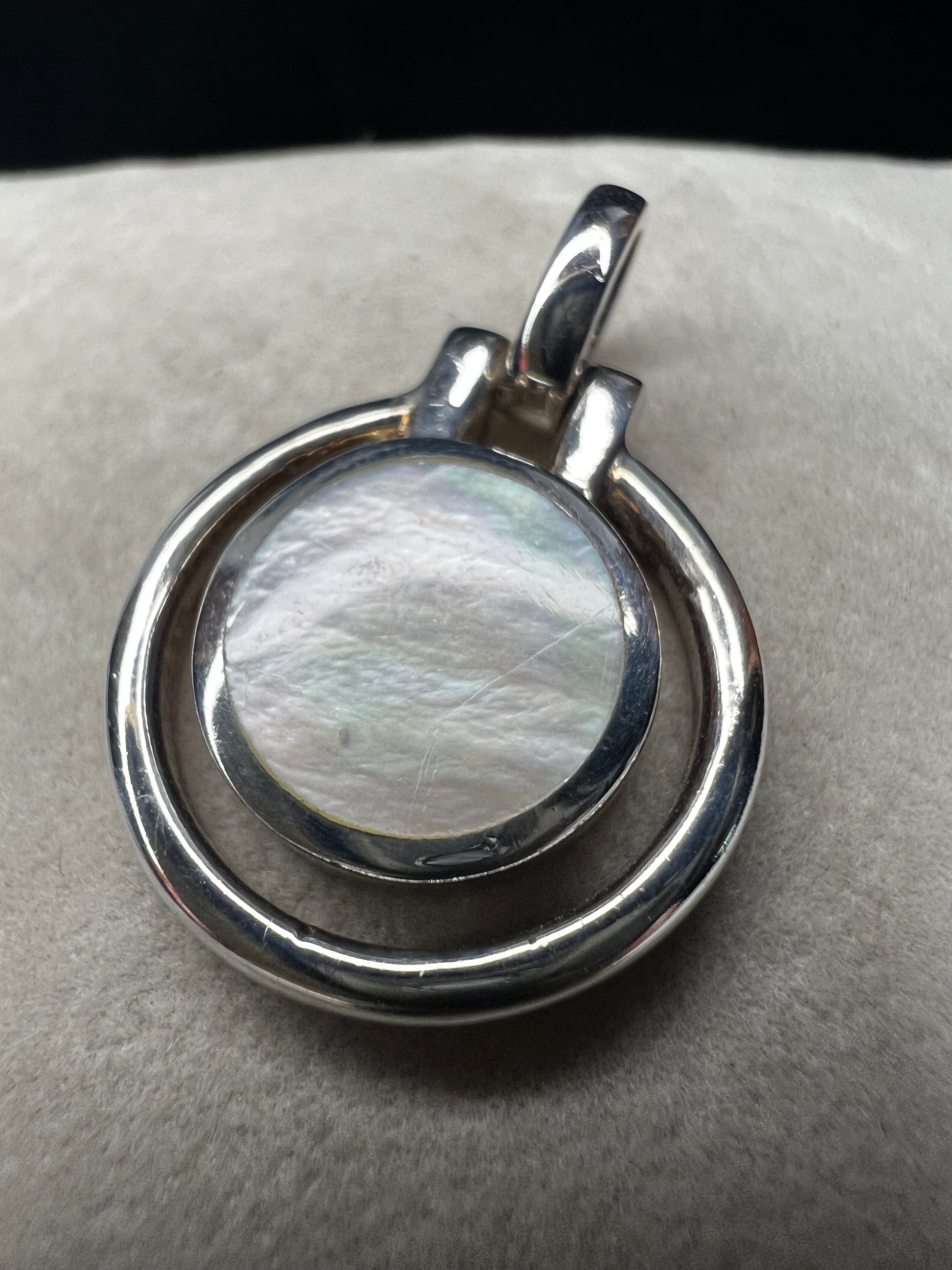 This sterling silver and mother of pearl pendant features a seamless design where the outer ring and bail are crafted as a single unit. The circular shape highlights the natural iridescence of the mother of pearl.