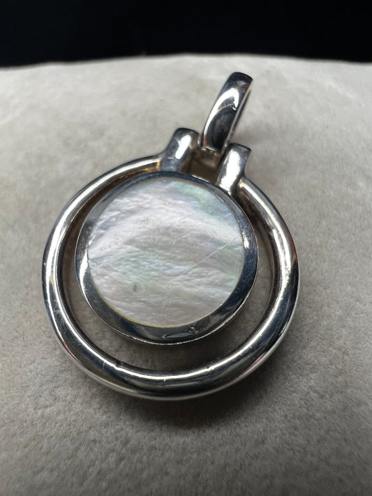 This sterling silver and mother of pearl pendant features a seamless design where the outer ring and bail are crafted as a single unit. The circular shape highlights the natural iridescence of the mother of pearl.