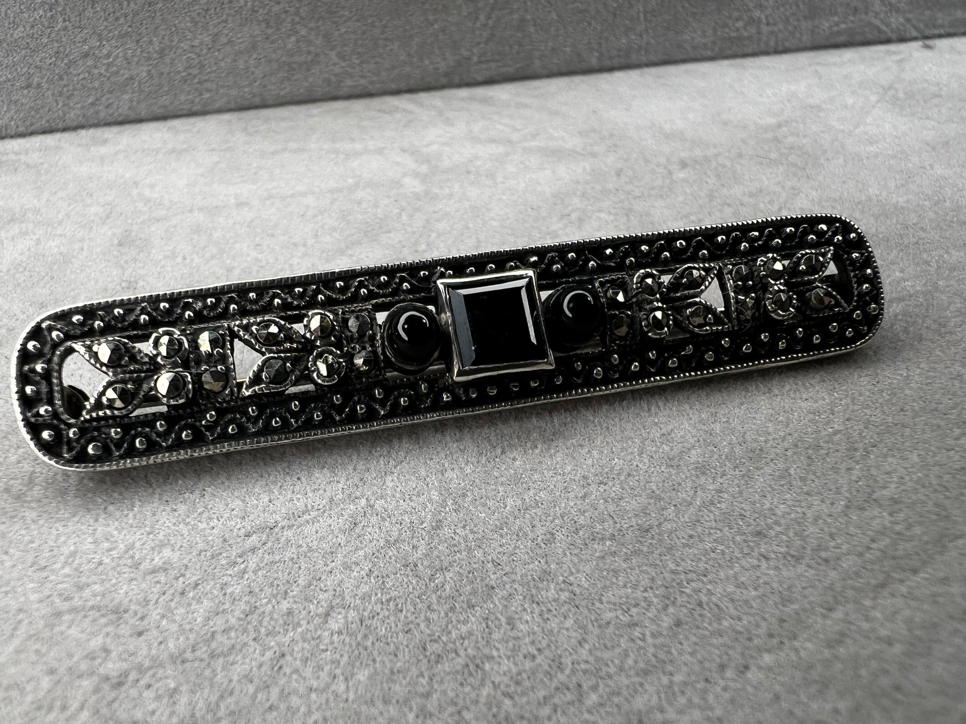 This exquisite 2-inch sterling silver bar brooch features authentic marcasite and jet stones, embodying the timeless elegance of the Art Deco era. It's a distinctive accessory that complements both vintage and modern styles.
