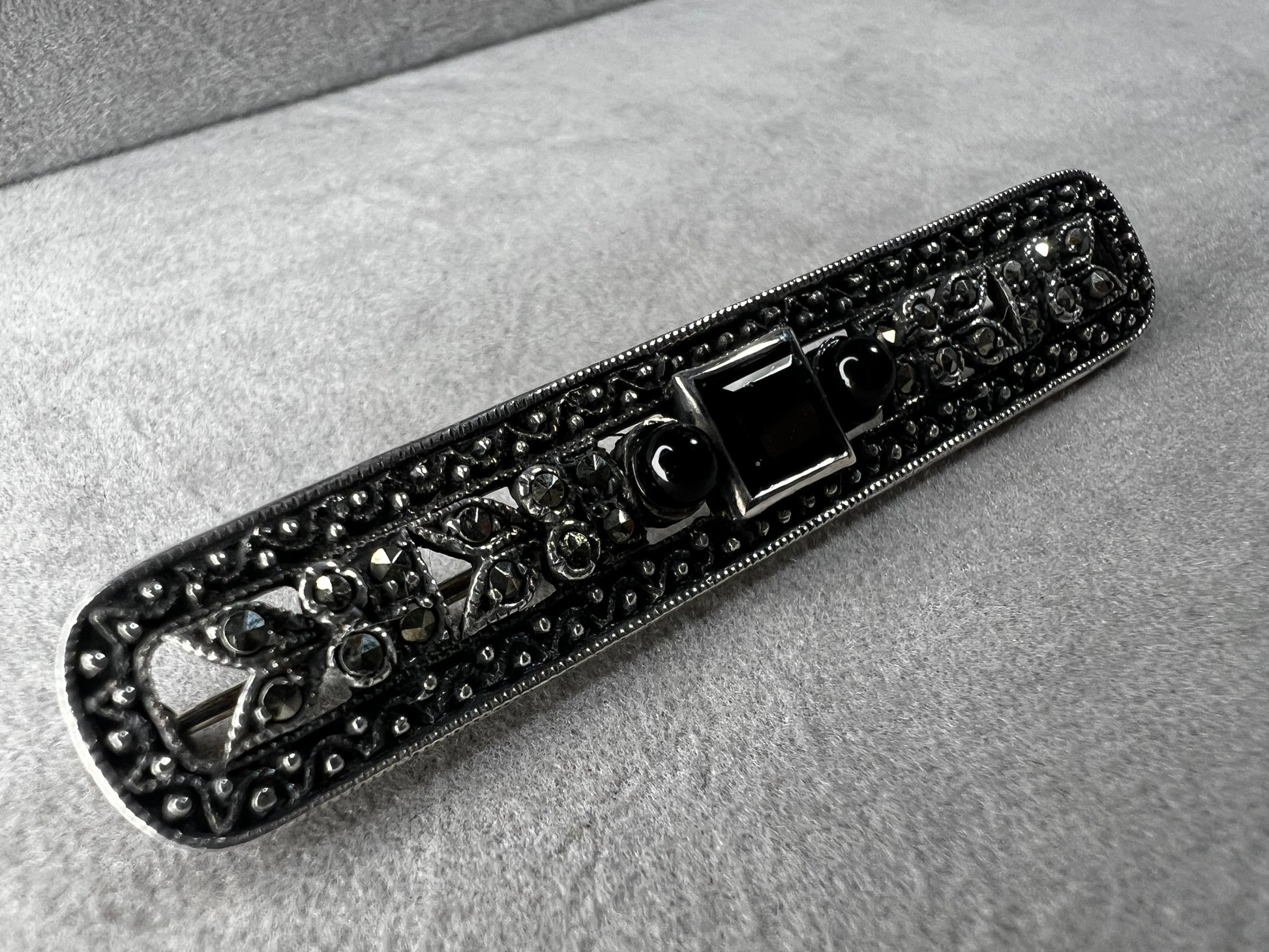 This exquisite 2-inch sterling silver bar brooch features authentic marcasite and jet stones, embodying the timeless elegance of the Art Deco era. It's a distinctive accessory that complements both vintage and modern styles.