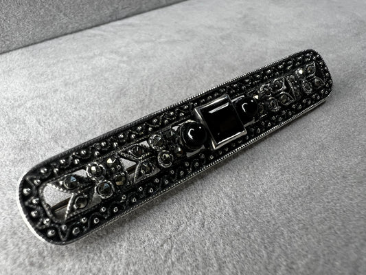 This exquisite 2-inch sterling silver bar brooch features authentic marcasite and jet stones, embodying the timeless elegance of the Art Deco era. It's a distinctive accessory that complements both vintage and modern styles.