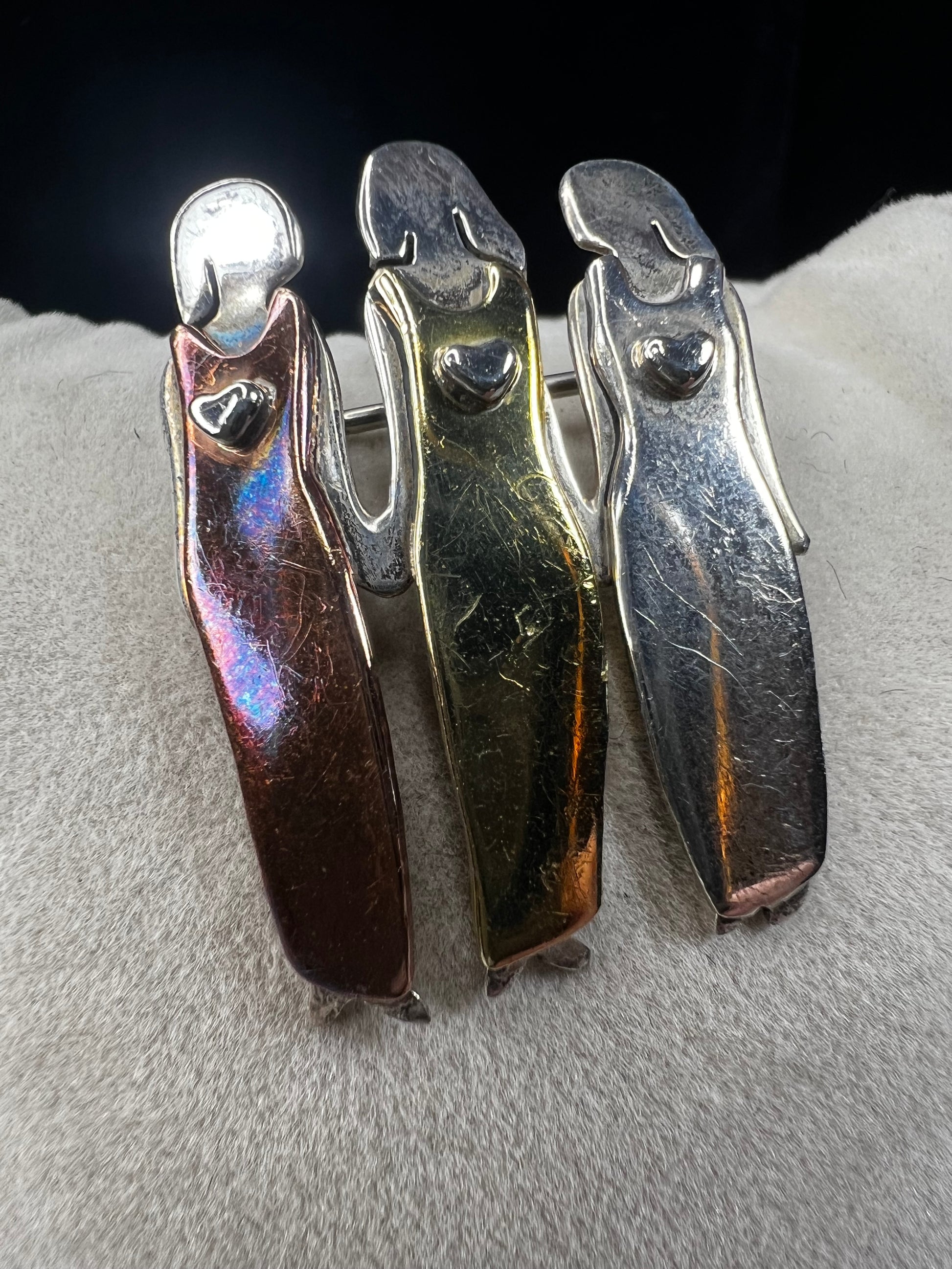 Signed "Far Fetched," this sterling silver pin features three women side by side, each wearing a different colored dress accented in brass, copper, and silver. A heartfelt design, it symbolizes friendship, sisterhood, and unity.