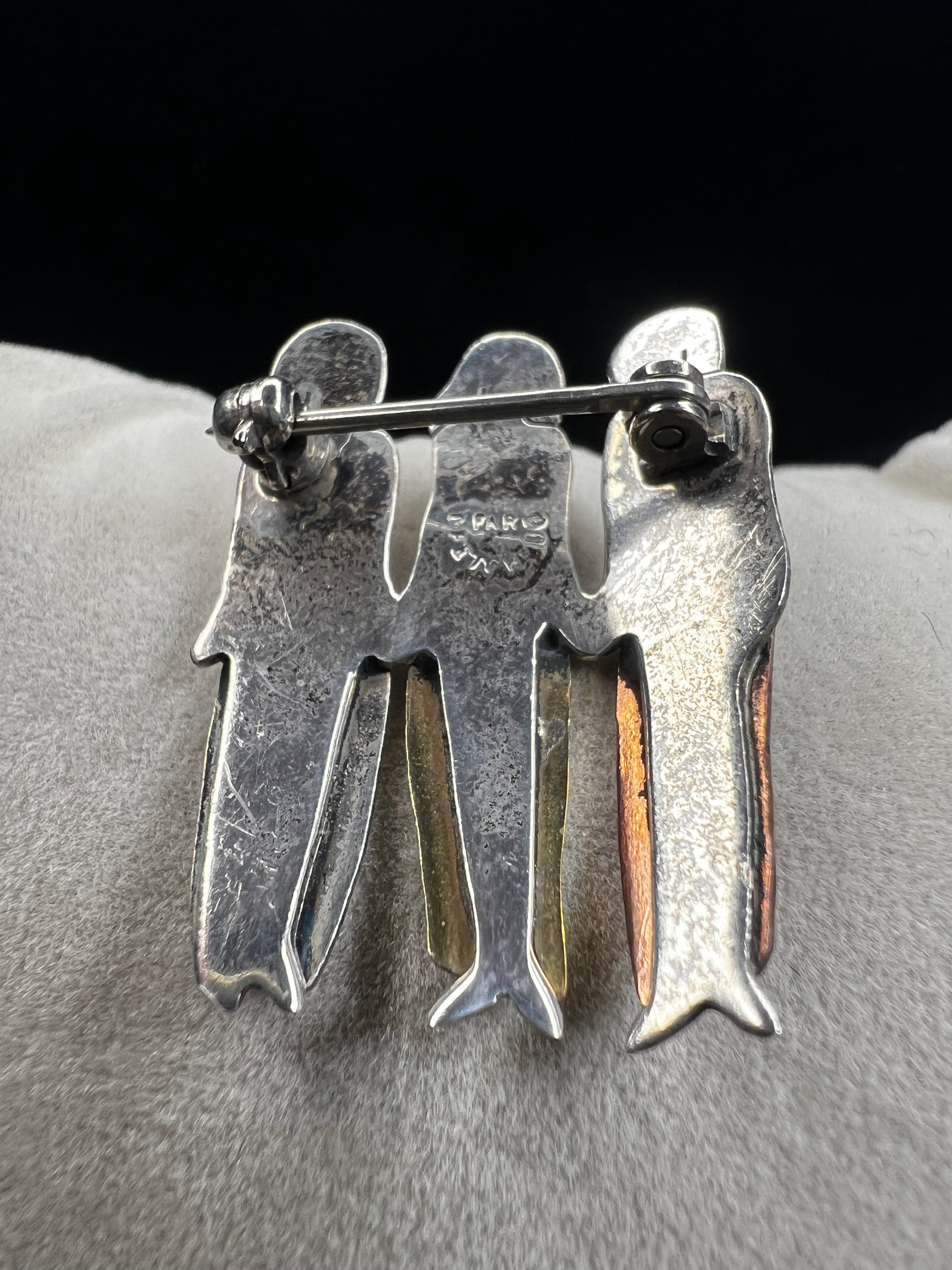 Signed "Far Fetched," this sterling silver pin features three women side by side, each wearing a different colored dress accented in brass, copper, and silver. A heartfelt design, it symbolizes friendship, sisterhood, and unity.
