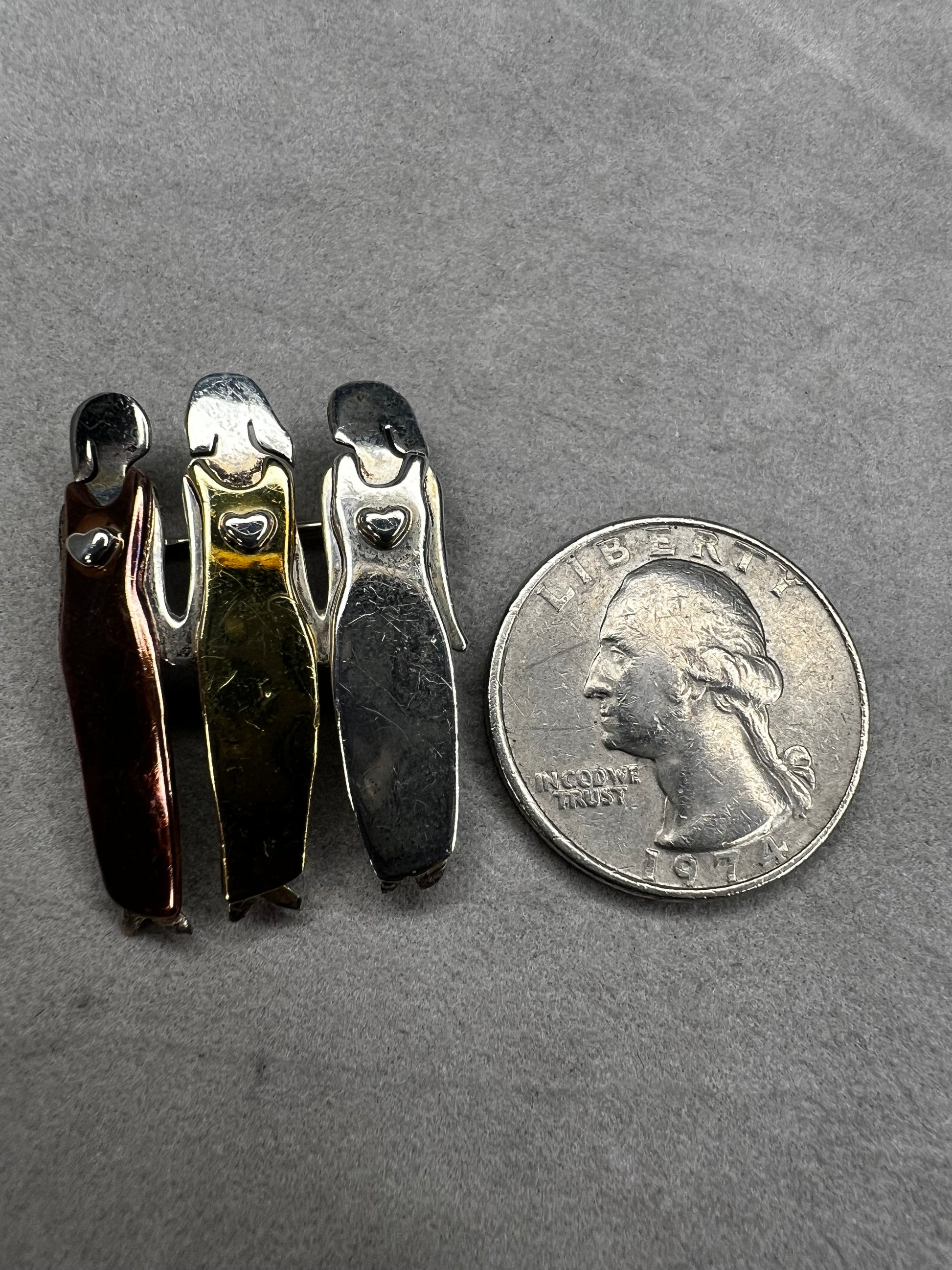Signed "Far Fetched," this sterling silver pin features three women side by side, each wearing a different colored dress accented in brass, copper, and silver. A heartfelt design, it symbolizes friendship, sisterhood, and unity.