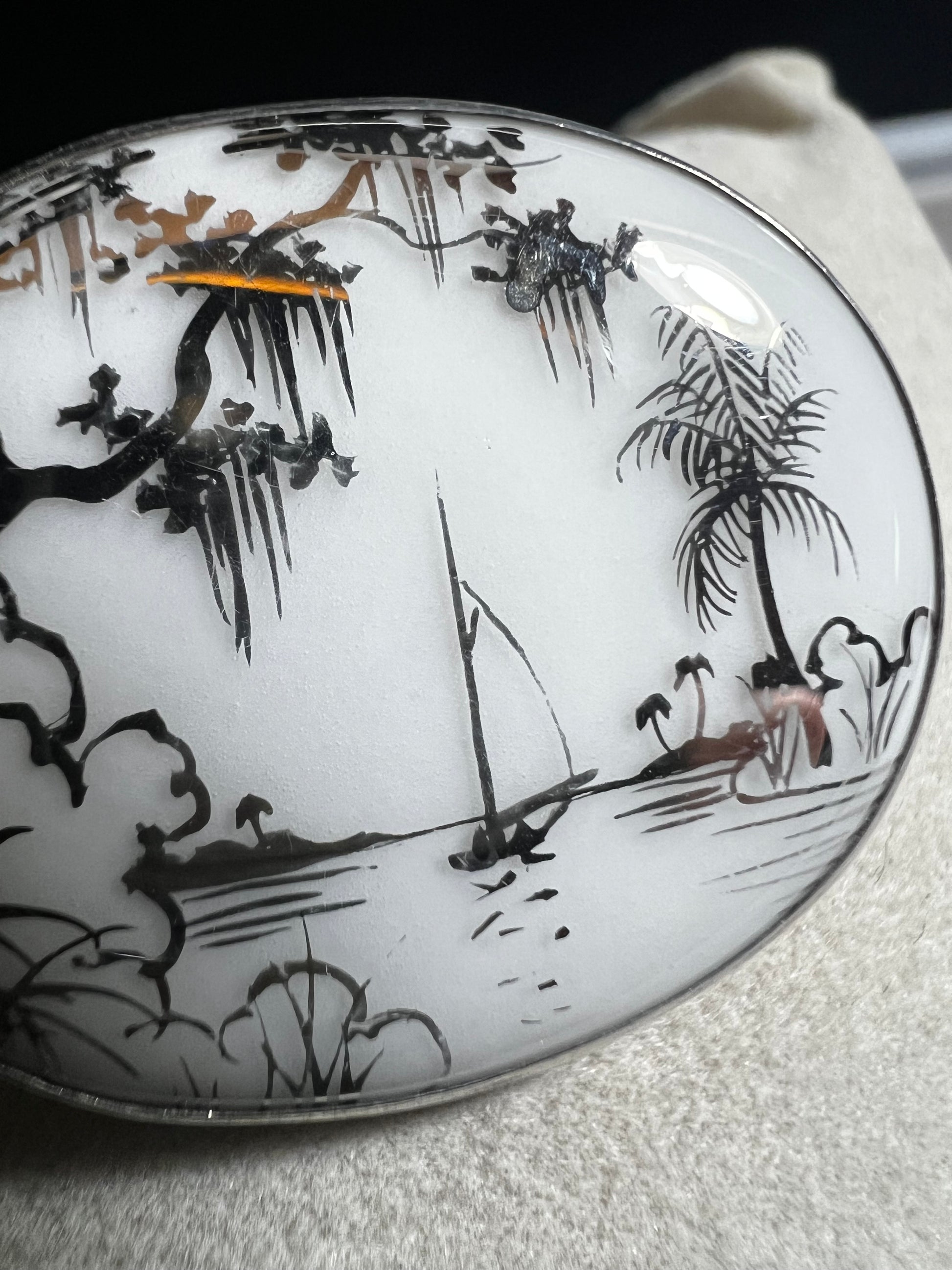 This vintage brooch is an original “cameona” by Florida artist Olive Commons, featuring a hand-painted porcelain scene of a sailboat and palms in her signature black linework with metallic accents. Commons coined the term cameona for these miniature painted landscapes, which became cherished Florida souvenirs and remain highly collectible today.
