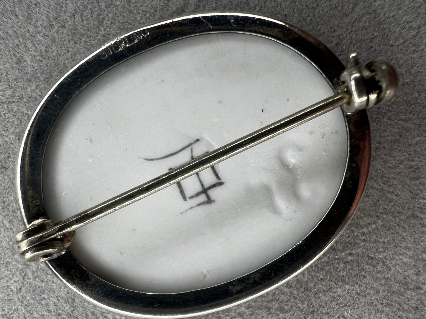 This vintage brooch is an original “cameona” by Florida artist Olive Commons, featuring a hand-painted porcelain scene of a sailboat and palms in her signature black linework with metallic accents. Commons coined the term cameona for these miniature painted landscapes, which became cherished Florida souvenirs and remain highly collectible today.