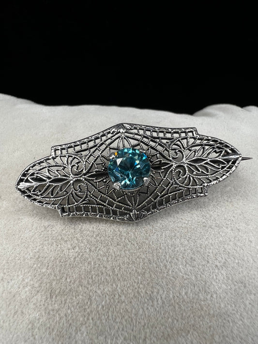 This antique filigree brooch features a beautiful blue topaz set in sterling silver, signed with a distinctive "K." Measuring 1.5 inches, it offers a delicate and elegant touch to any jewelry collection. Perfect for adding a vintage charm to your style.