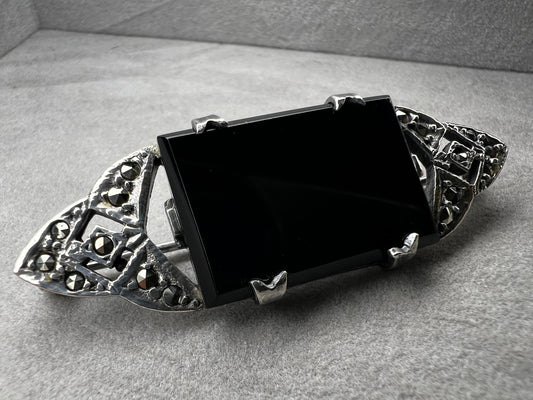 This vintage sterling silver brooch showcases a striking large rectangular onyx stone, beautifully complemented by marcasite accents on both openwork ends. Perfect for those who appreciate vintage charm and refined style.