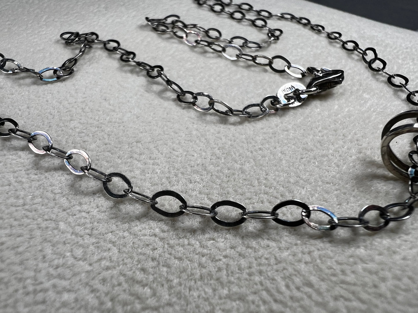 This striking pendant on a chain necklace features a polished Larvikite cabochon, showcasing its distinctive dark gray body with shimmering silver flashes. The stone is set in an artistic sterling silver wirework design, creating a bold and modern statement piece.