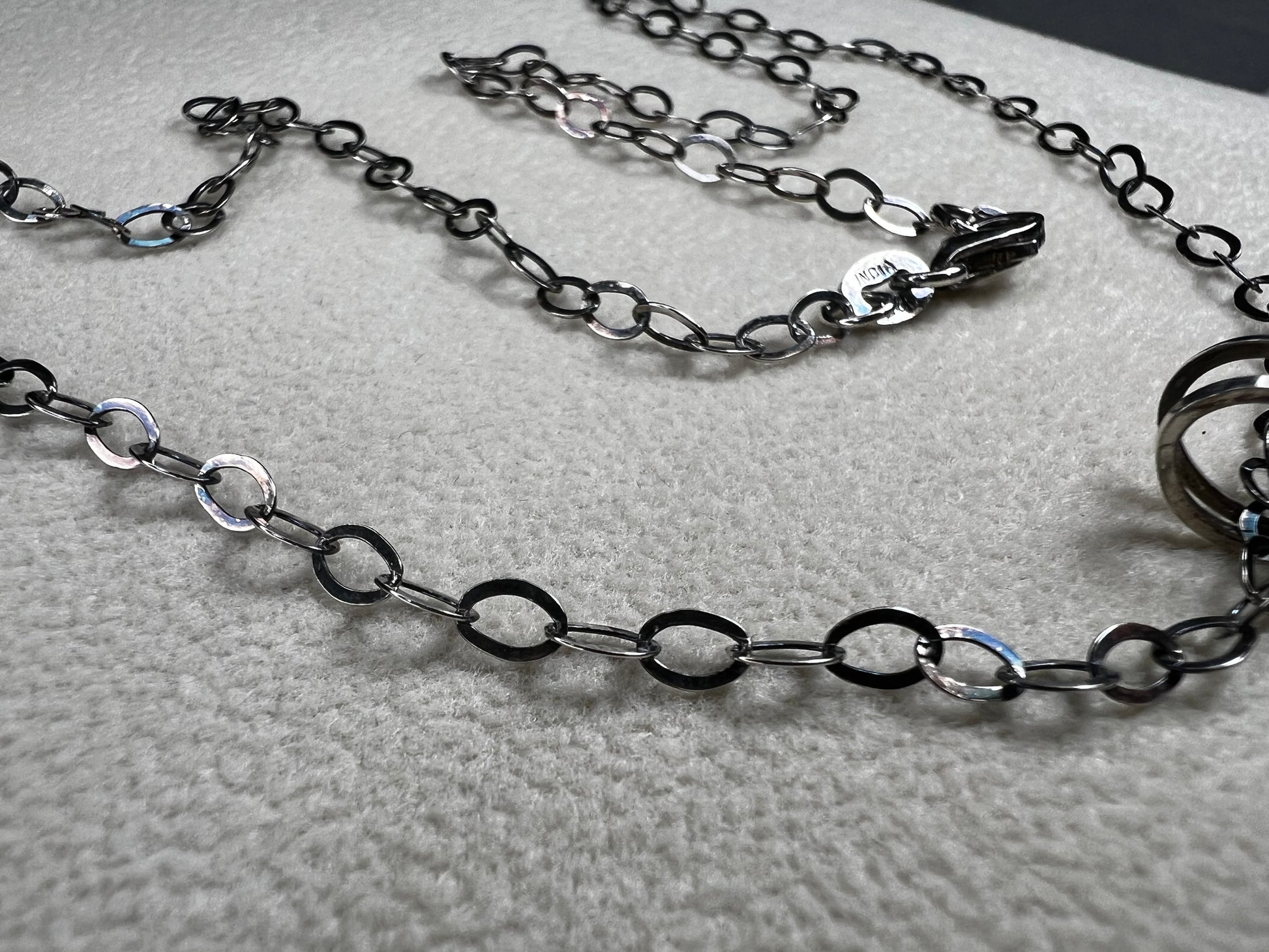 This striking pendant on a chain necklace features a polished Larvikite cabochon, showcasing its distinctive dark gray body with shimmering silver flashes. The stone is set in an artistic sterling silver wirework design, creating a bold and modern statement piece.