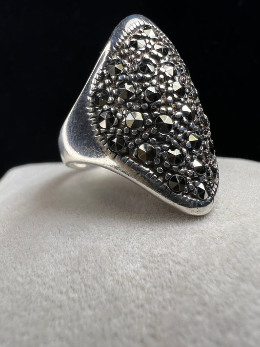 This striking vintage ring makes a bold statement with its wide, shield-shaped design. Crafted from sterling silver, the piece is beautifully set with glittering faceted marcasite stones, creating a dramatic sparkle that catches the light from every angle.