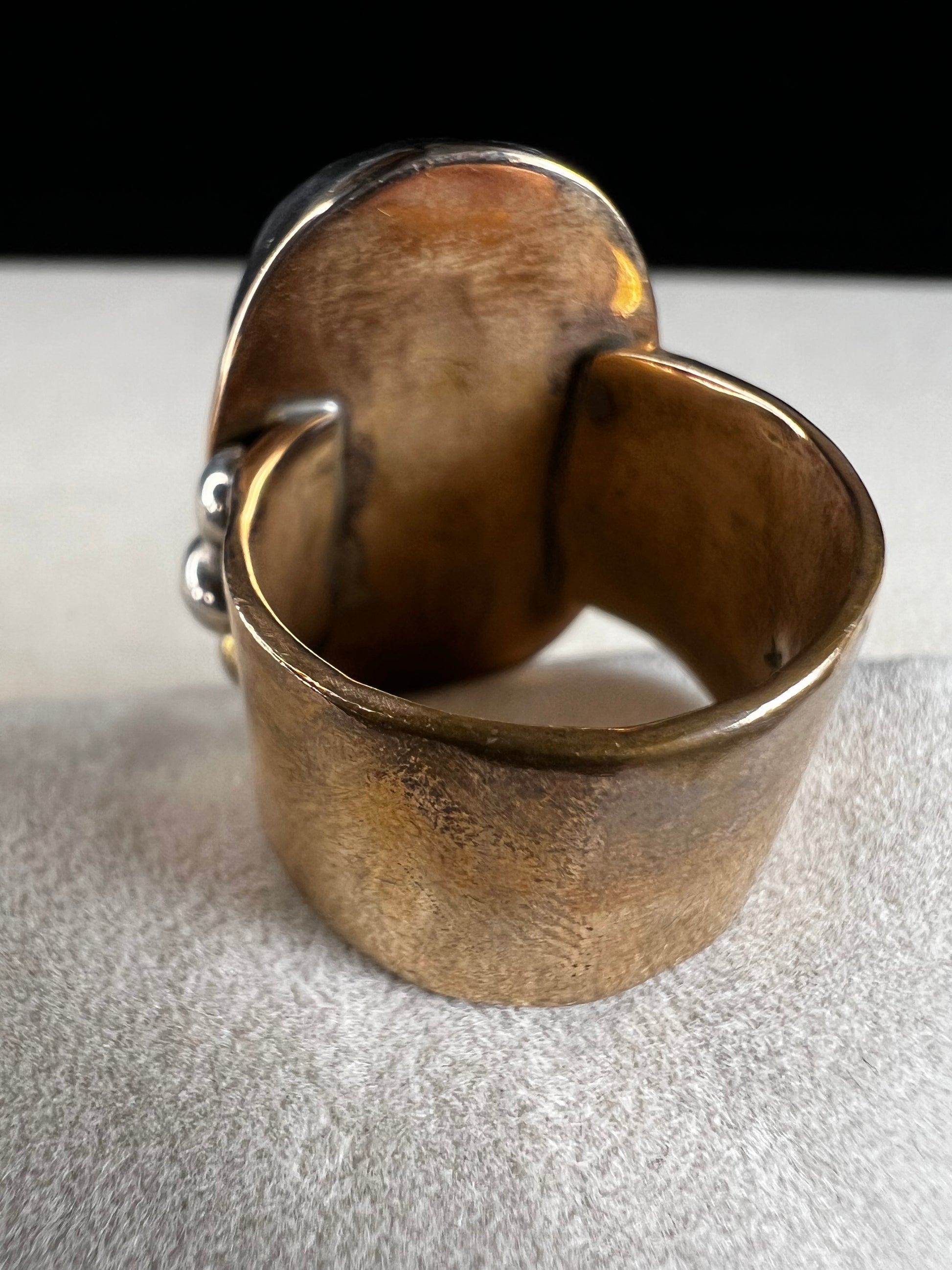 This ring by Loving Anvil features a dendritic limestone cabochon, which displays striking fern-like black inclusions that resemble a natural landscape. The stone is set in sterling silver against a brass band with a thin overlay of gold.