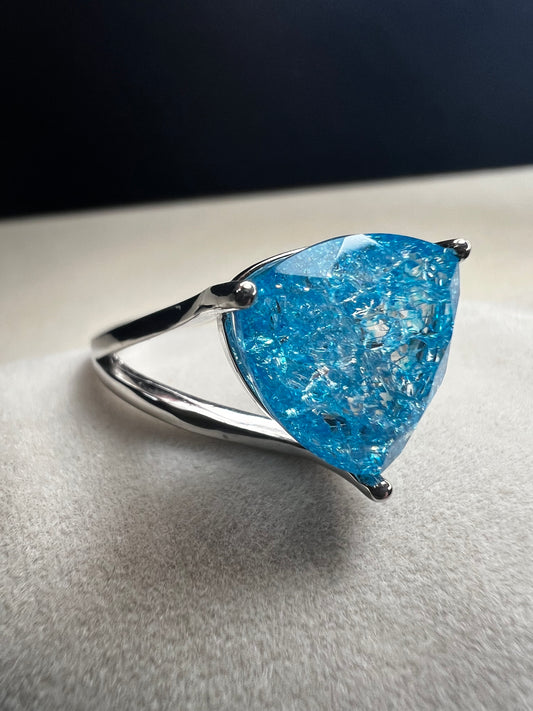 This sterling silver ring showcases a large, blue trilliant cut crackled quartz, creating a captivating centerpiece. Perfect for adding a touch of elegance and distinctiveness to any outfit.