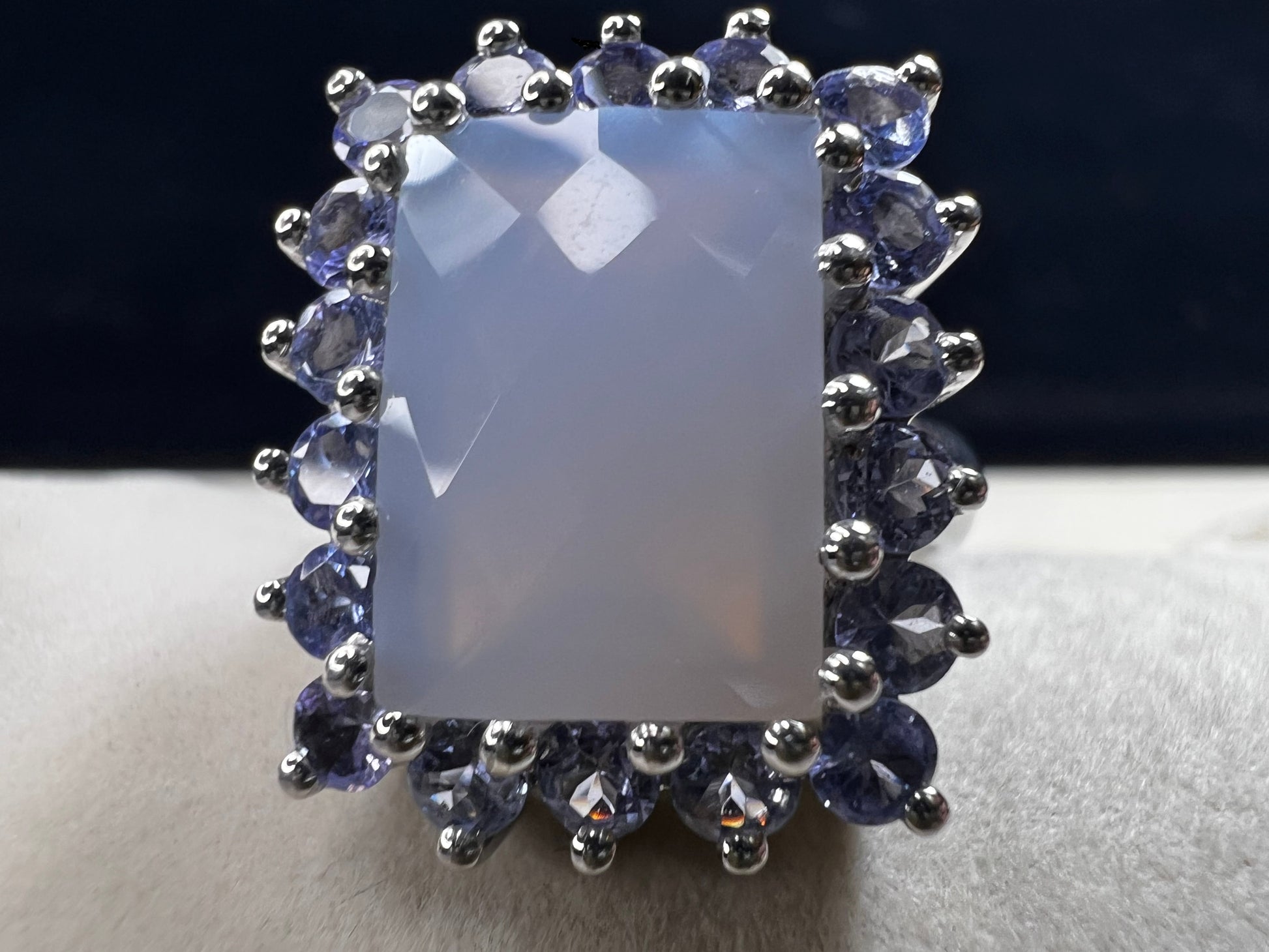 This sterling silver ring combines comfortable wear with captivating style. Featuring a large chalcedony centerpiece surrounded by sparkling tanzanite accent stones, this piece offers a stunning and elegant look.