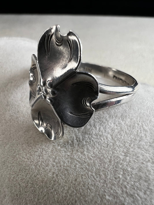 This sterling silver ring by Stuart Nye showcases a delicate dogwood flower design, combining artistry with elegant craftsmanship. Its refined detail makes it a meaningful accessory that adds a touch of nature-inspired beauty to any outfit.
