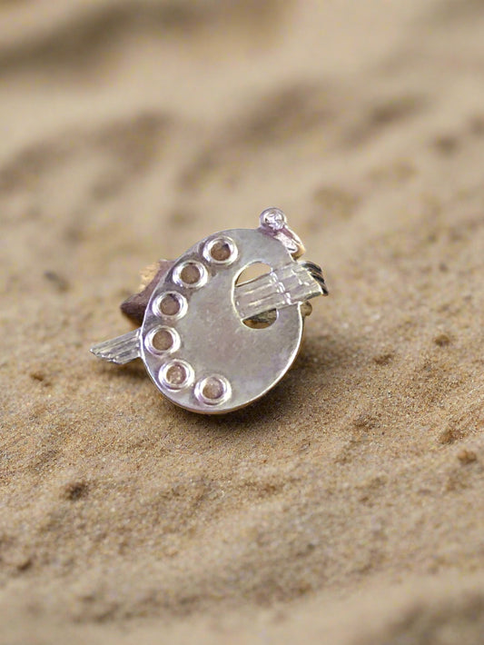 This sterling silver charm is crafted as a paint palette, making it perfect for an artist who knows their way around a blank canvas. Its total length is approximately 7/8" and, at its widest, is 5/8". Total weight: 2.4 grams.