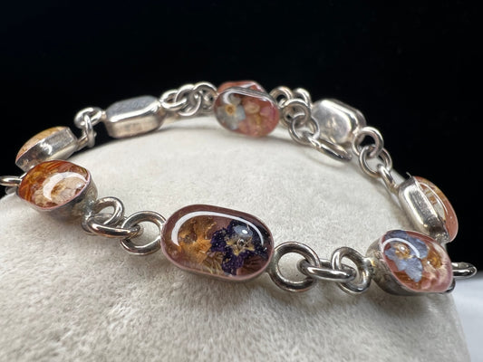 Add a touch of vintage beauty to your outfit with this sterling silver bracelet. Adorned with dried flowers encased in resin cabochons, this unique bracelet will let you bring a piece of nature with you everywhere you go.