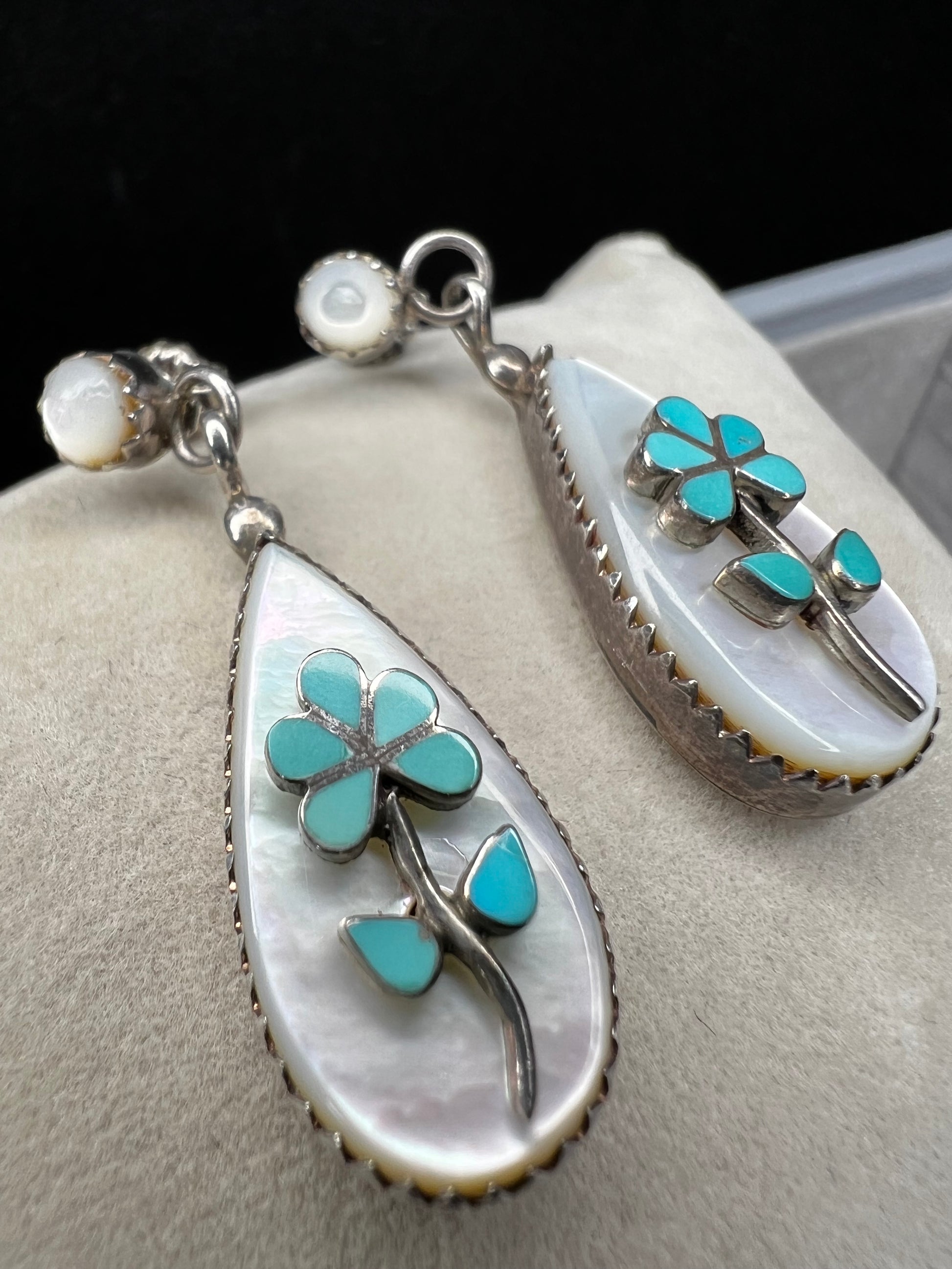 These handmade Zuni sterling silver earrings feature raised turquoise flowers set over luminous mother of pearl. Signed CL Zuni, these teardrop earrings showcase traditional Native American artistry with beautiful depth and dimension.
