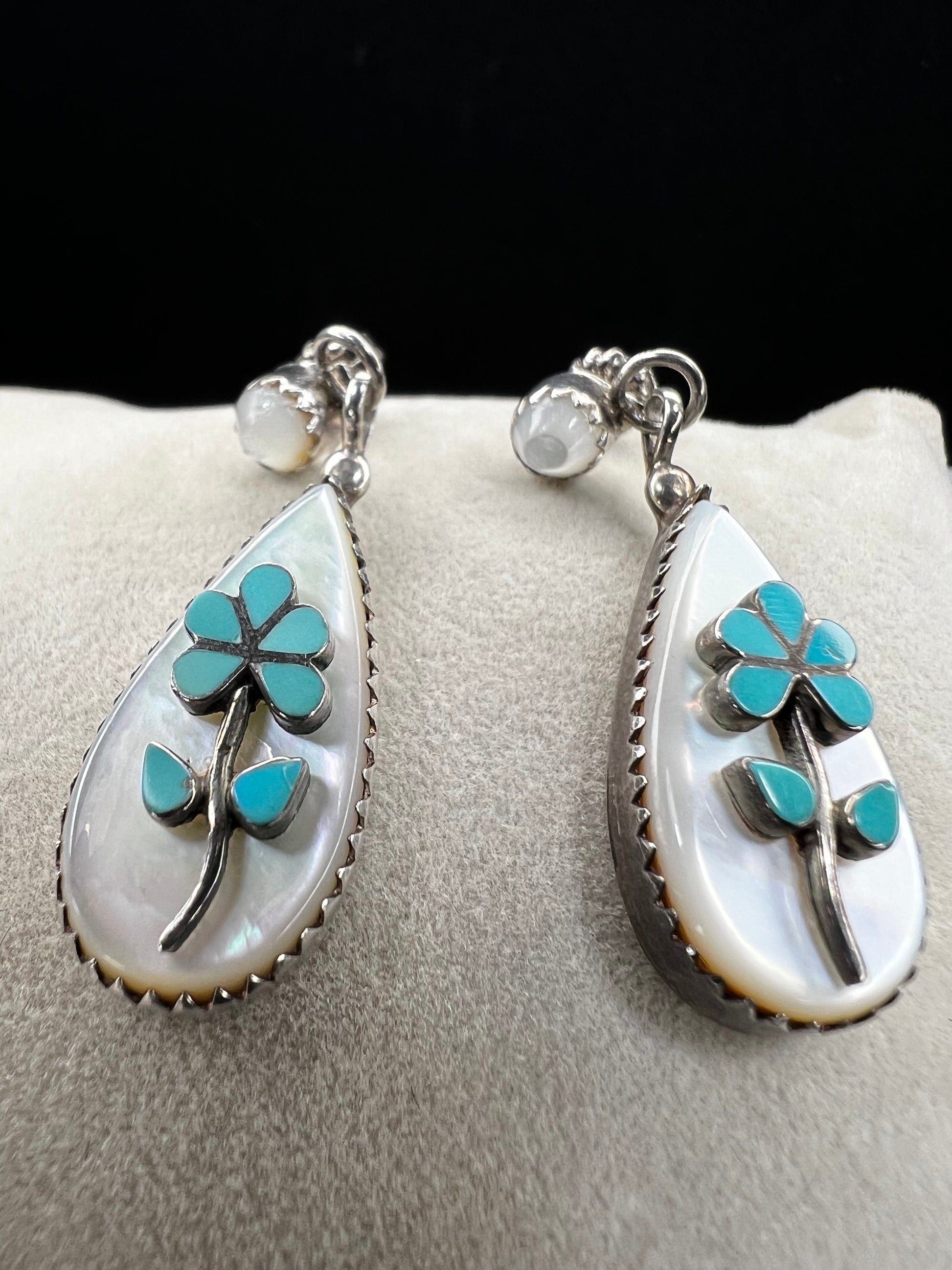 These handmade Zuni sterling silver earrings feature raised turquoise flowers set over luminous mother of pearl. Signed CL Zuni, these teardrop earrings showcase traditional Native American artistry with beautiful depth and dimension.