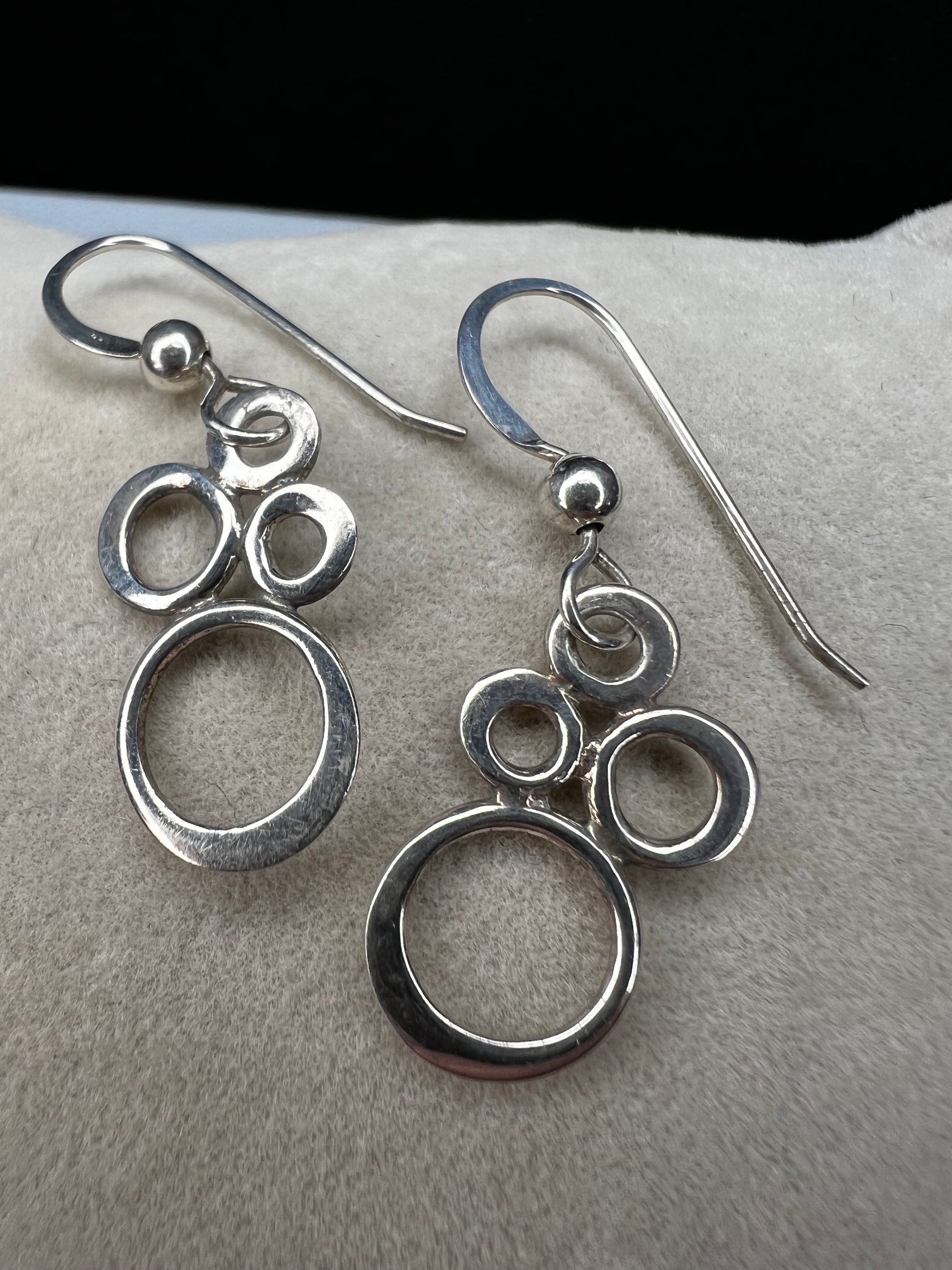 These elegant sterling silver dangle earrings feature an eye-catching arrangement of circles in varying sizes, creating a playful yet minimalist look.