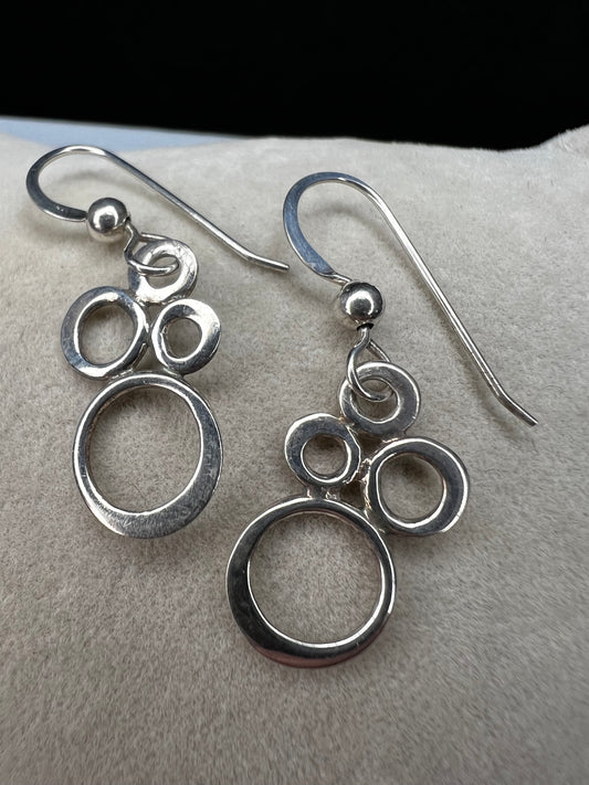 These elegant sterling silver dangle earrings feature an eye-catching arrangement of circles in varying sizes, creating a playful yet minimalist look.