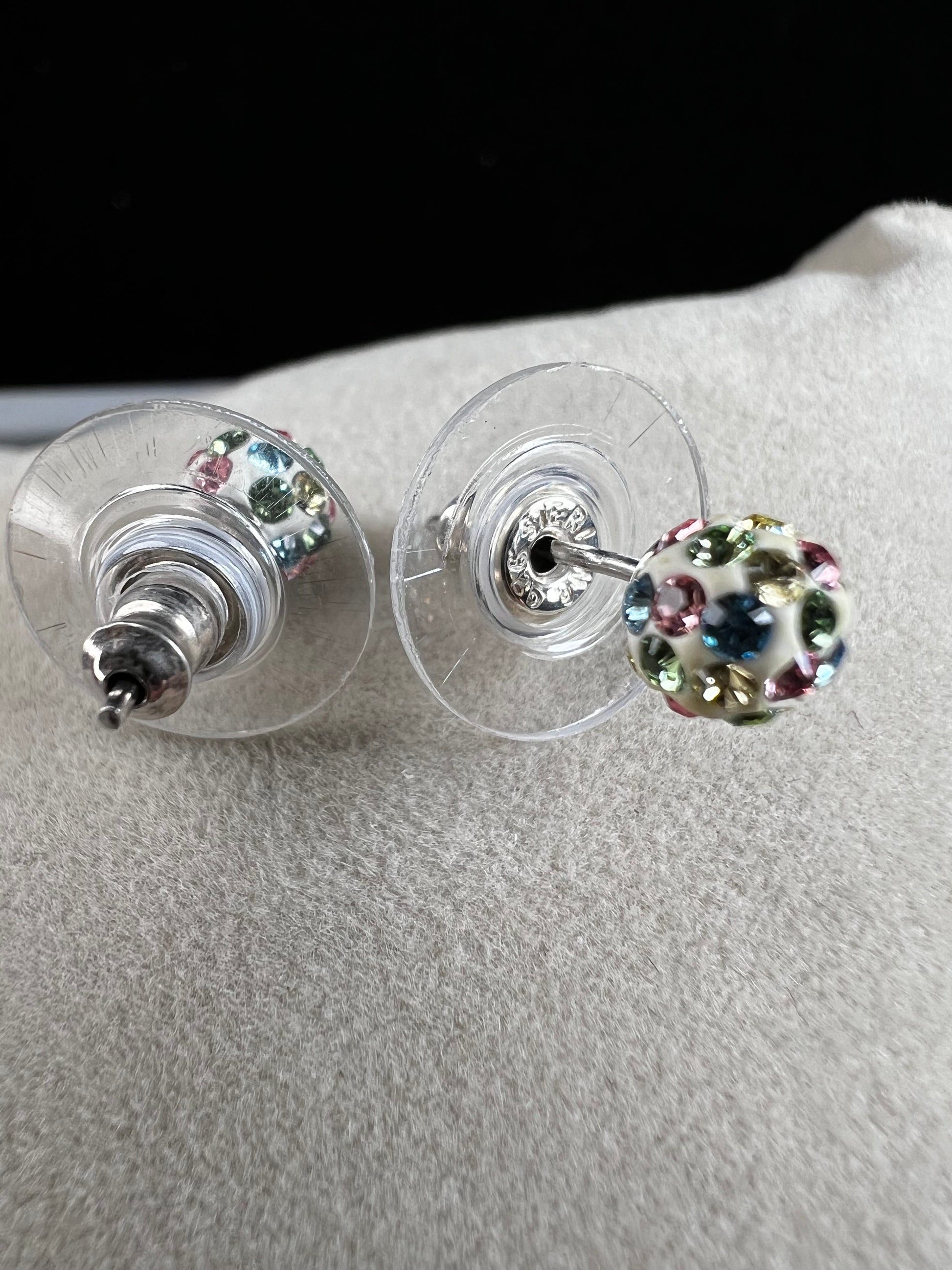 Crafted from sterling silver, these stud earrings are detailed with white enamel and sprinkled with crystals in a variety of colors that create a vibrant sparkle.
