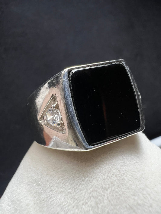 This vintage Avon ring showcases a prominent onyx cabochon flanked by two small cubic zirconias. Designed in a larger size, it is suitable for both men and women.