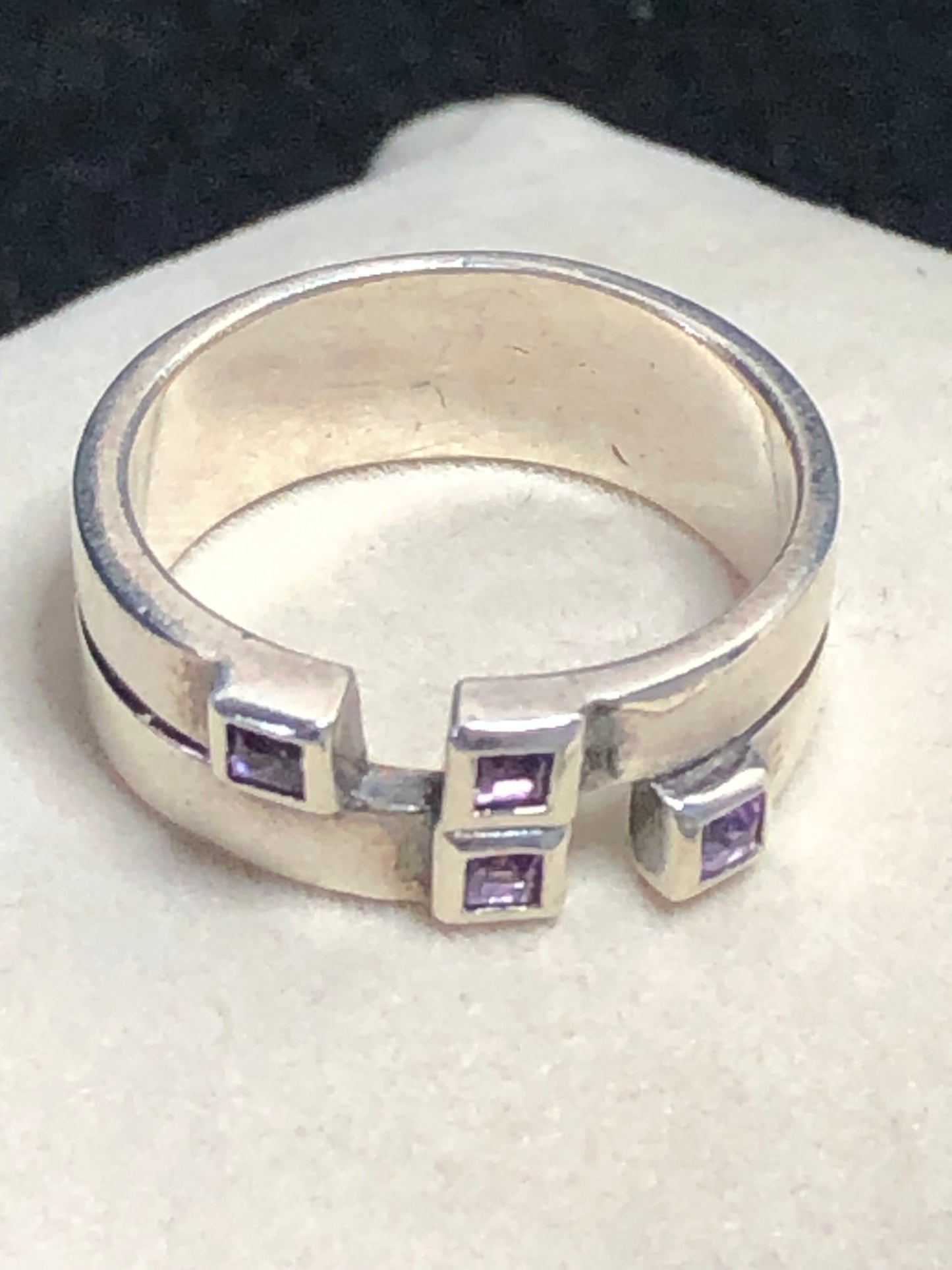 This sterling silver ring features a wide band expertly designed to resemble two distinct bands, creating a unique and sophisticated aesthetic. Adorned with vibrant amethyst stones, it offers expert craftsmanship and a refined look.