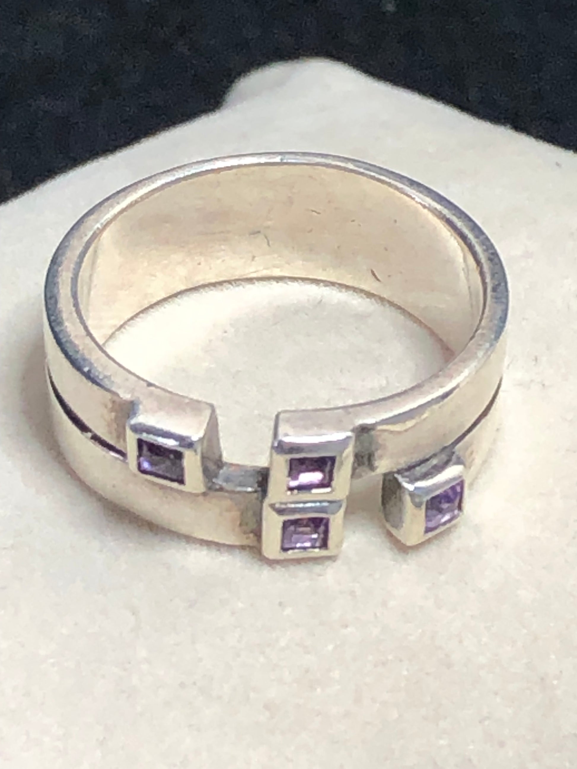 This sterling silver ring features a wide band expertly designed to resemble two distinct bands, creating a unique and sophisticated aesthetic. Adorned with vibrant amethyst stones, it offers expert craftsmanship and a refined look.