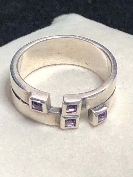This sterling silver ring features a wide band expertly designed to resemble two distinct bands, creating a unique and sophisticated aesthetic. Adorned with vibrant amethyst stones, it offers expert craftsmanship and a refined look.