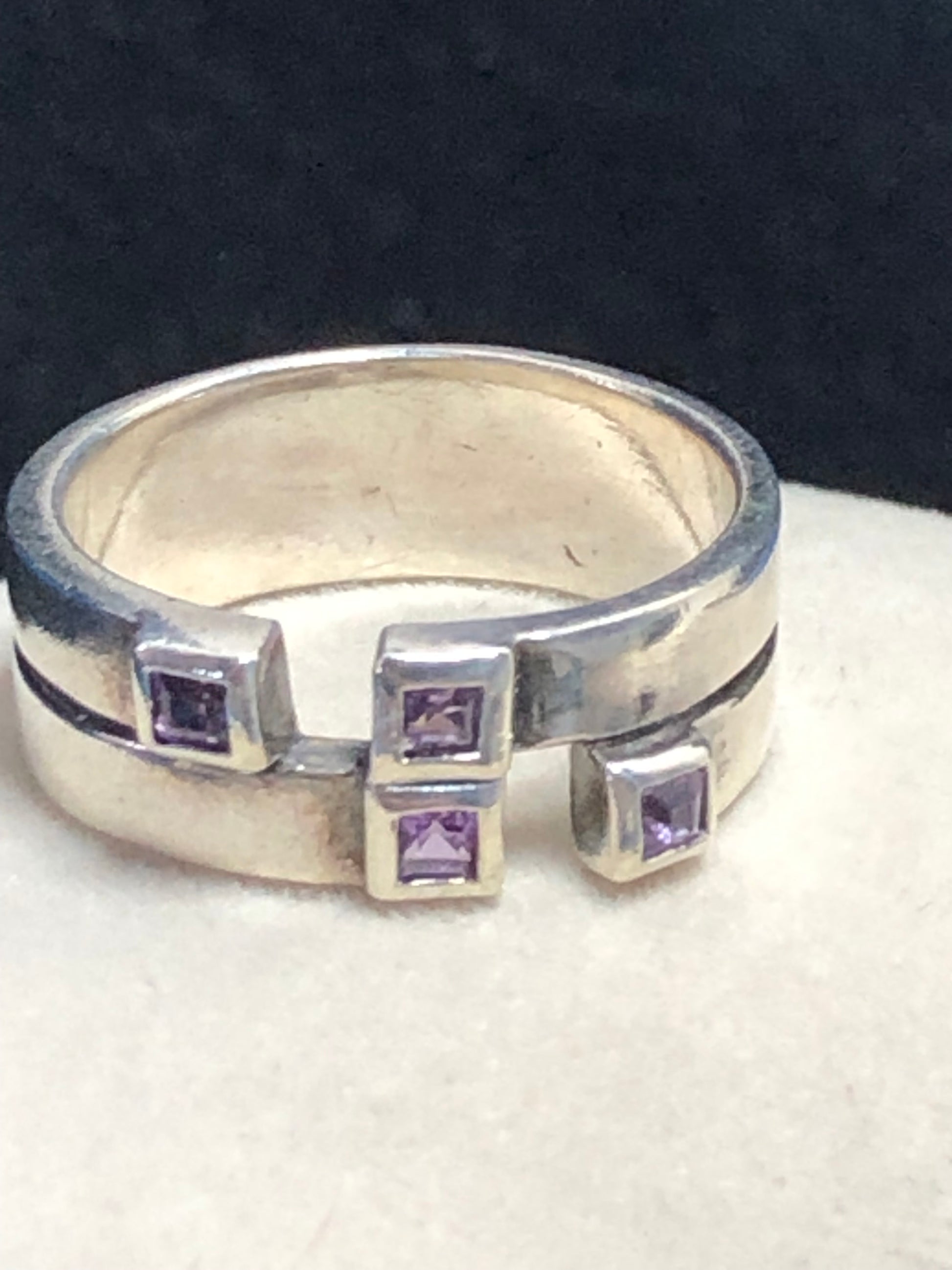 This sterling silver ring features a wide band expertly designed to resemble two distinct bands, creating a unique and sophisticated aesthetic. Adorned with vibrant amethyst stones, it offers expert craftsmanship and a refined look.