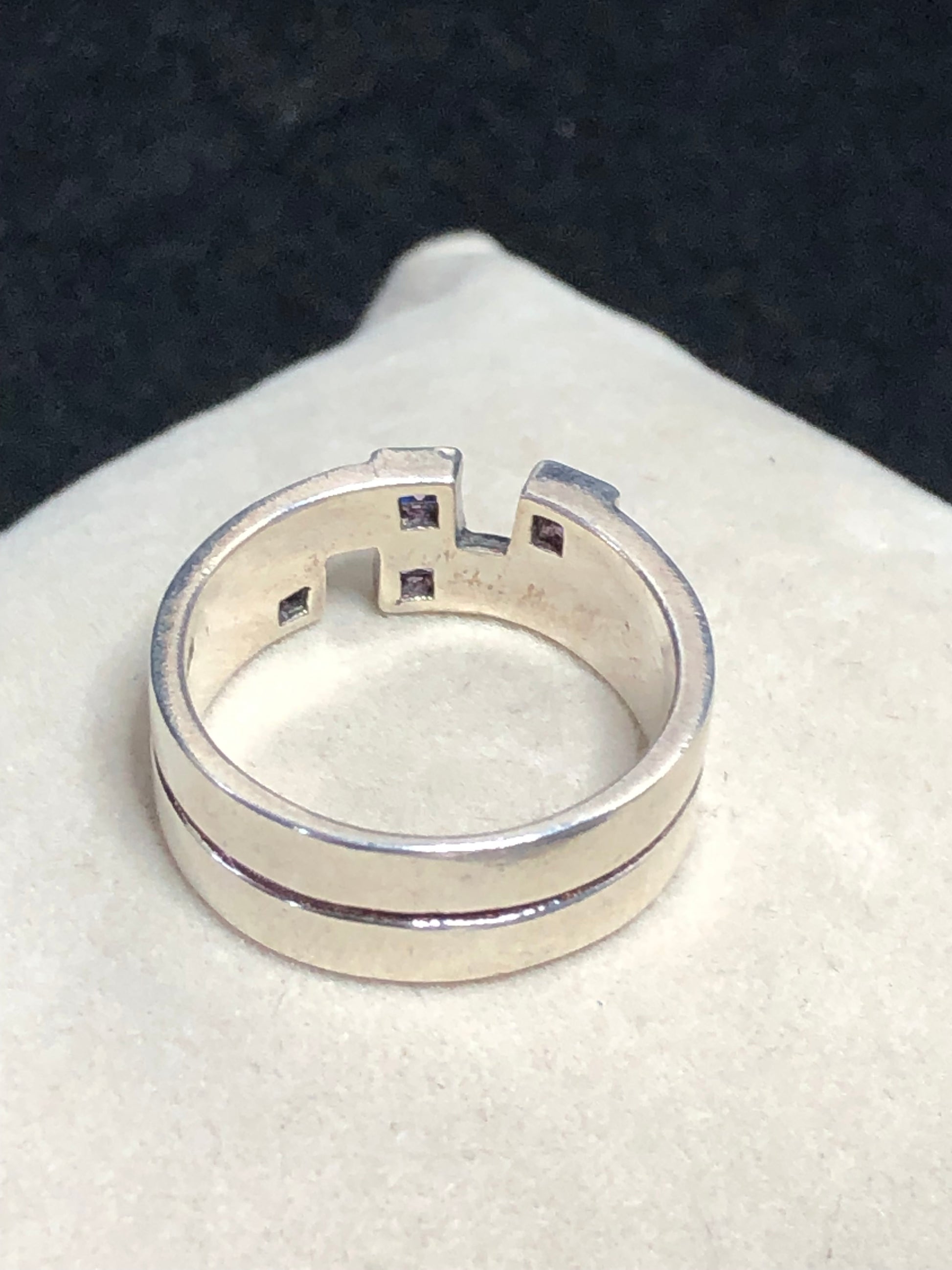 This sterling silver ring features a wide band expertly designed to resemble two distinct bands, creating a unique and sophisticated aesthetic. Adorned with vibrant amethyst stones, it offers expert craftsmanship and a refined look.