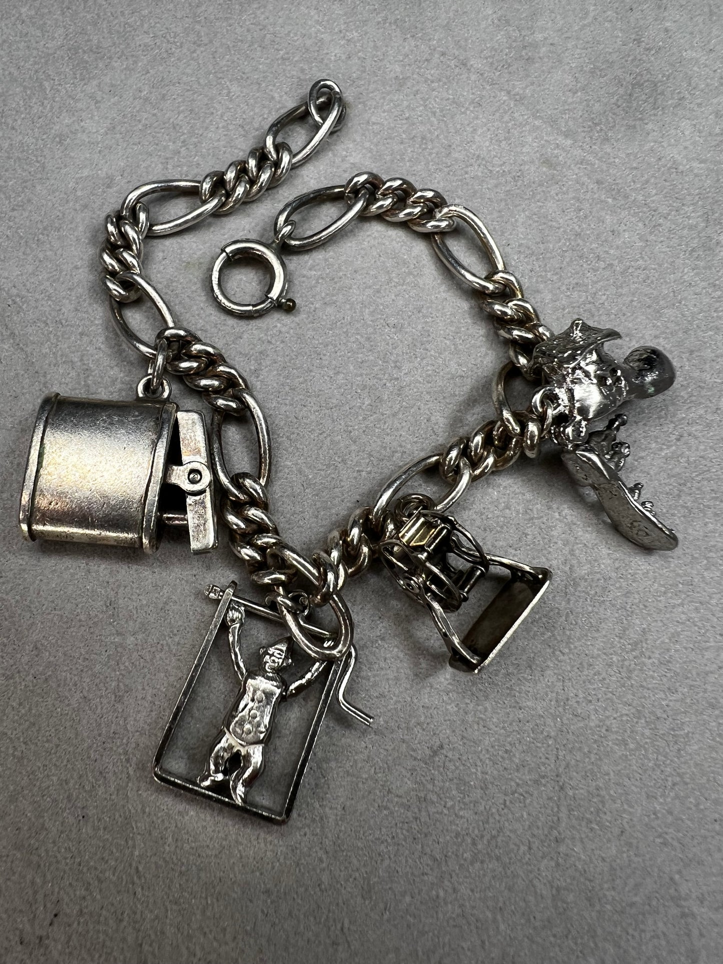 This 1940s sterling silver bracelet features four articulated charms: a Ferris wheel, a gymnastics clown, the old woman in a shoe, and a lighter. Each charm is finely crafted, showcasing detailed workmanship characteristic of the era.