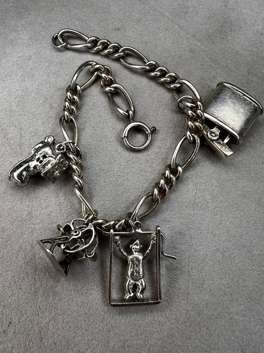 This 1940s sterling silver bracelet features four articulated charms: a Ferris wheel, a gymnastics clown, the old woman in a shoe, and a lighter. Each charm is finely crafted, showcasing detailed workmanship characteristic of the era.