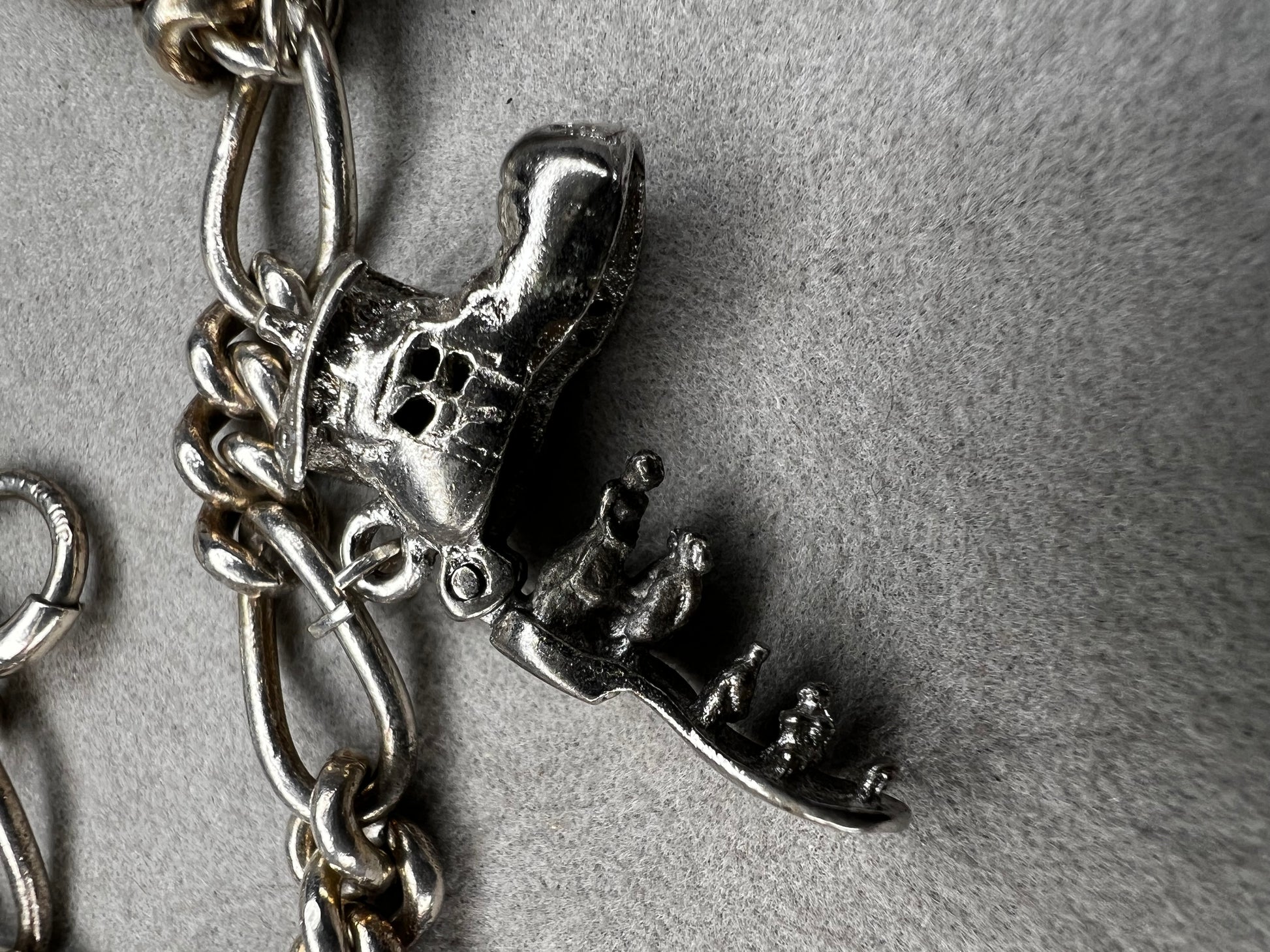 This 1940s sterling silver bracelet features four articulated charms: a Ferris wheel, a gymnastics clown, the old woman in a shoe, and a lighter. Each charm is finely crafted, showcasing detailed workmanship characteristic of the era.