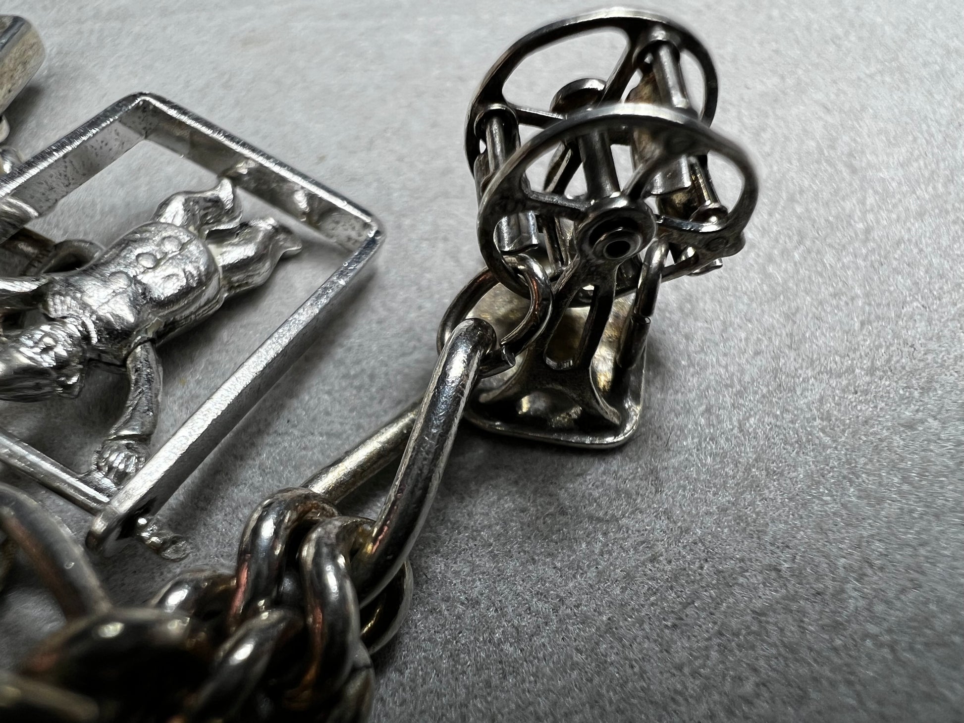 This 1940s sterling silver bracelet features four articulated charms: a Ferris wheel, a gymnastics clown, the old woman in a shoe, and a lighter. Each charm is finely crafted, showcasing detailed workmanship characteristic of the era.