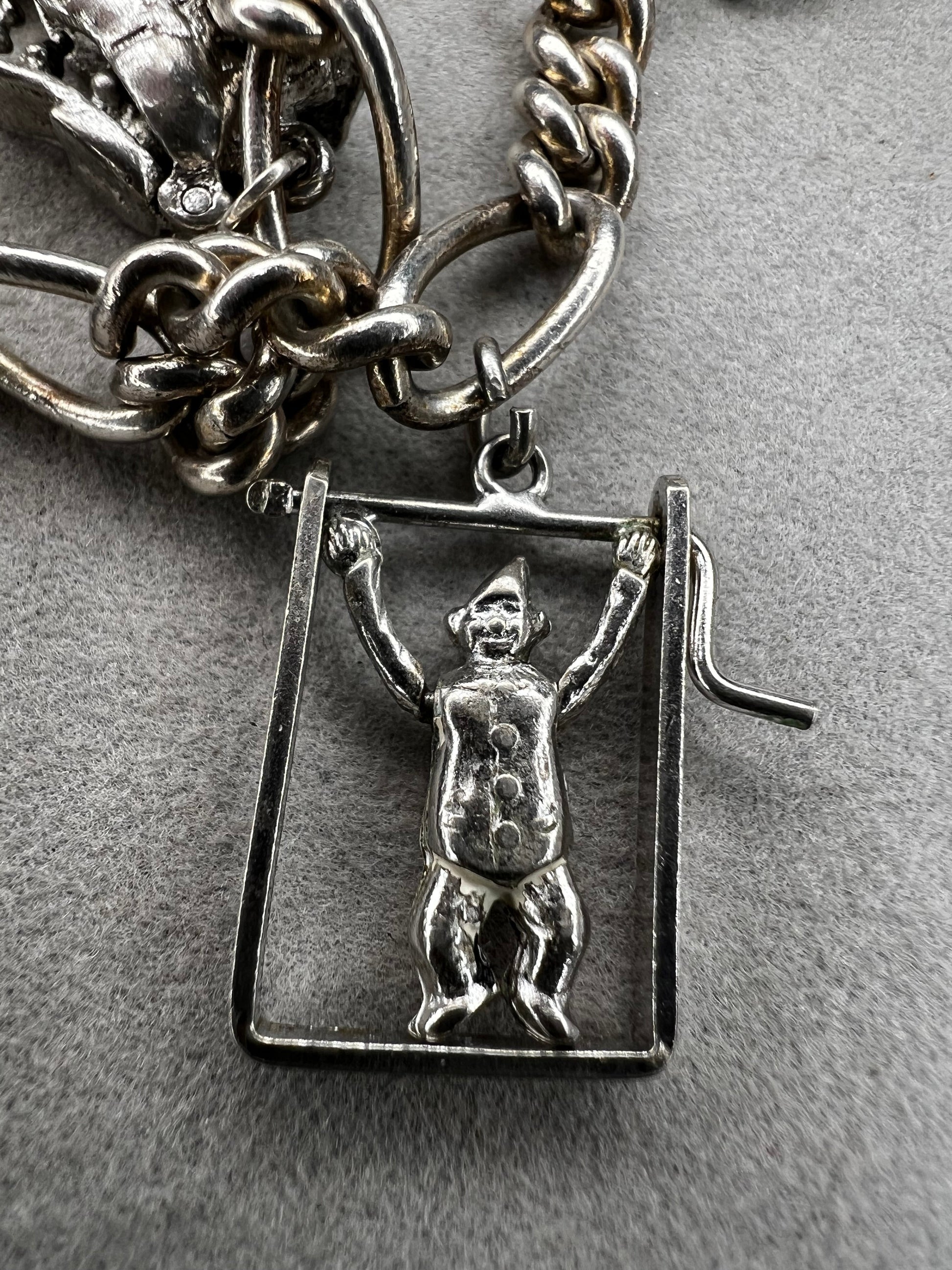 This 1940s sterling silver bracelet features four articulated charms: a Ferris wheel, a gymnastics clown, the old woman in a shoe, and a lighter. Each charm is finely crafted, showcasing detailed workmanship characteristic of the era.