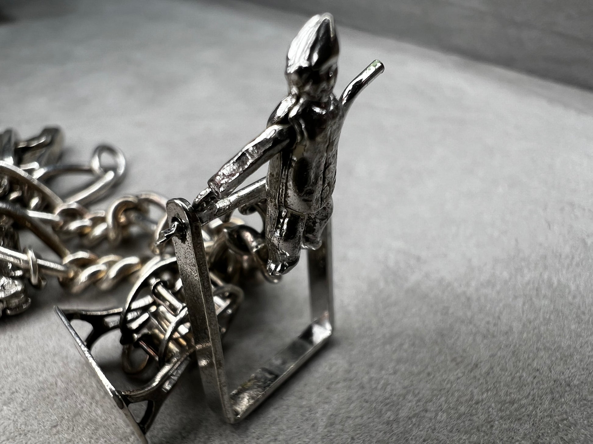 This 1940s sterling silver bracelet features four articulated charms: a Ferris wheel, a gymnastics clown, the old woman in a shoe, and a lighter. Each charm is finely crafted, showcasing detailed workmanship characteristic of the era.