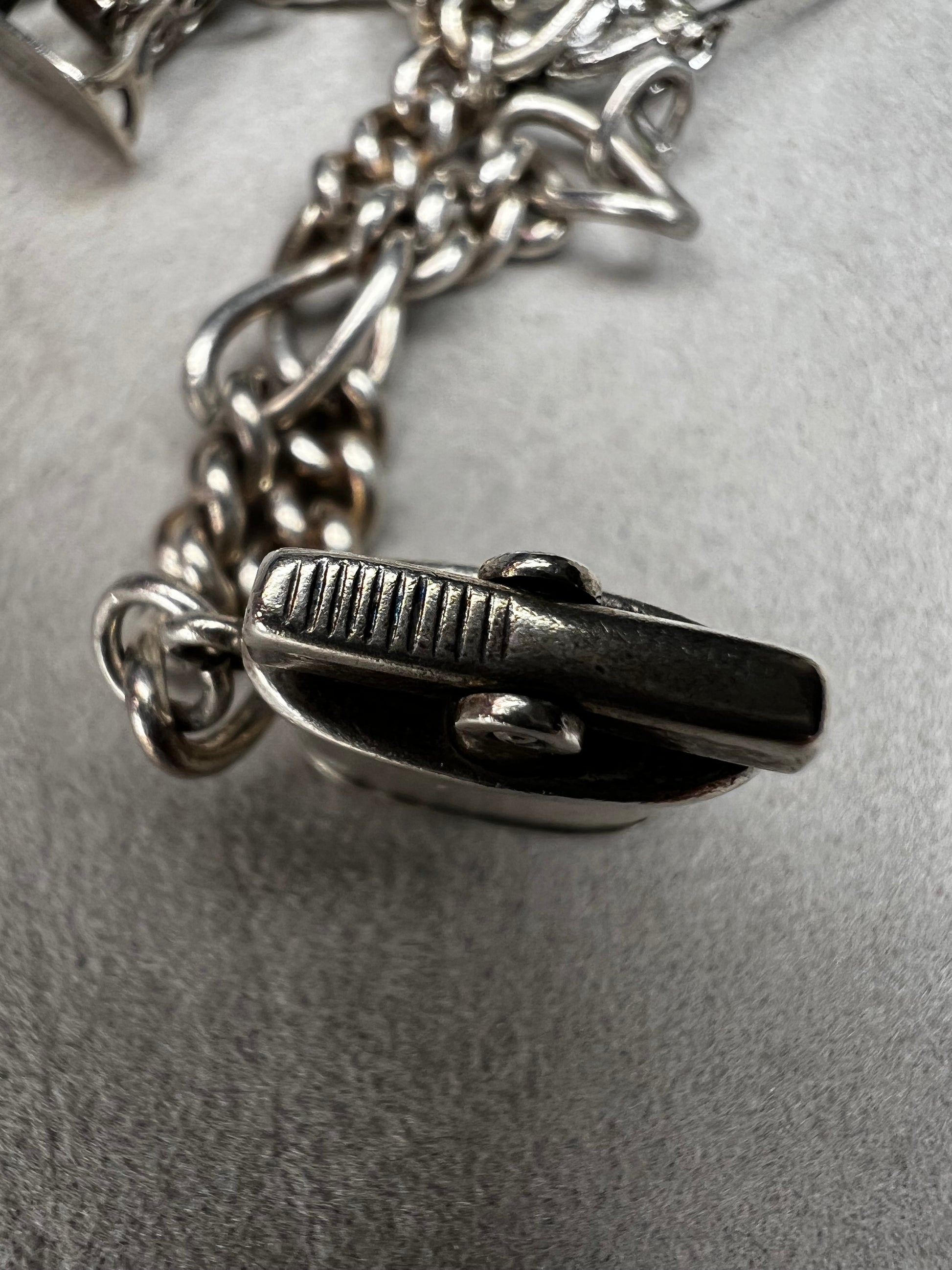 This 1940s sterling silver bracelet features four articulated charms: a Ferris wheel, a gymnastics clown, the old woman in a shoe, and a lighter. Each charm is finely crafted, showcasing detailed workmanship characteristic of the era.