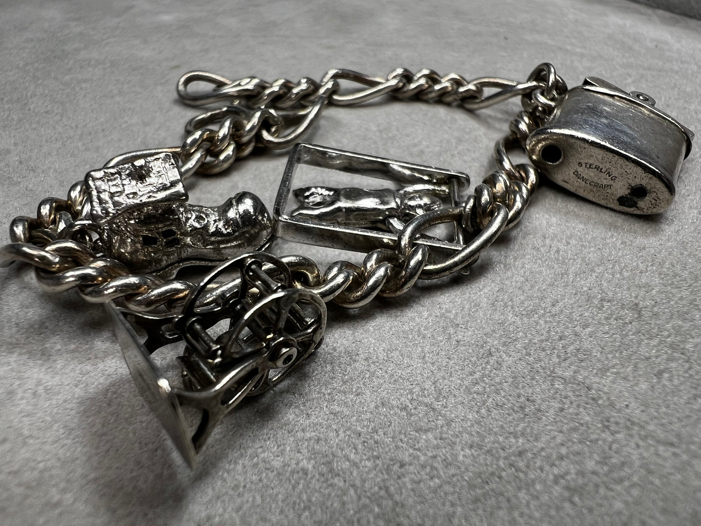 This 1940s sterling silver bracelet features four articulated charms: a Ferris wheel, a gymnastics clown, the old woman in a shoe, and a lighter. Each charm is finely crafted, showcasing detailed workmanship characteristic of the era.