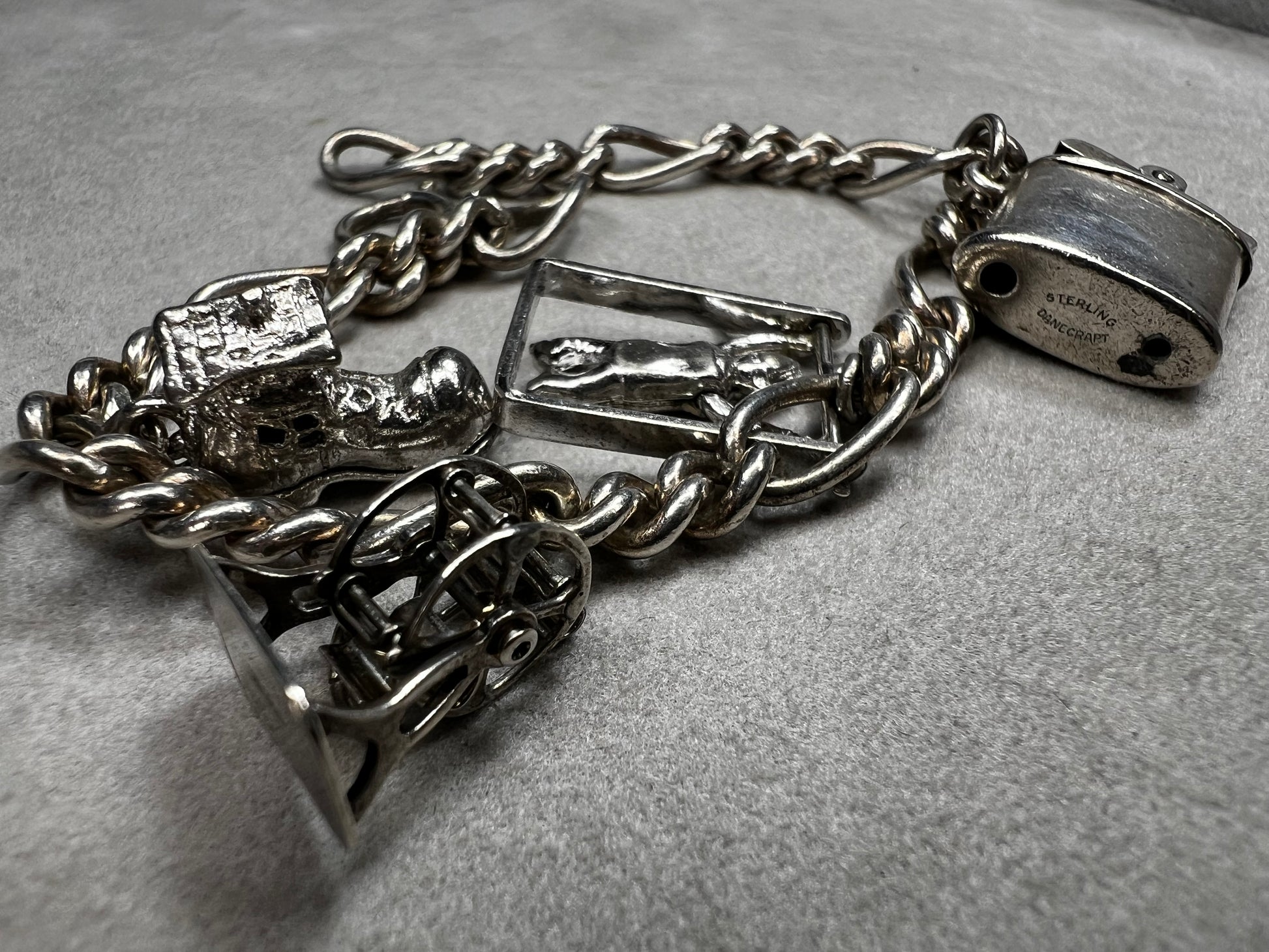 This 1940s sterling silver bracelet features four articulated charms: a Ferris wheel, a gymnastics clown, the old woman in a shoe, and a lighter. Each charm is finely crafted, showcasing detailed workmanship characteristic of the era.