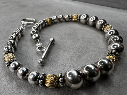 This sterling silver bracelet showcases a refined design with graduated beads, six of which are accented by a gold overlay. The contrasting two-tone finish adds depth and elegance, making it a versatile accessory for both casual and formal wear.