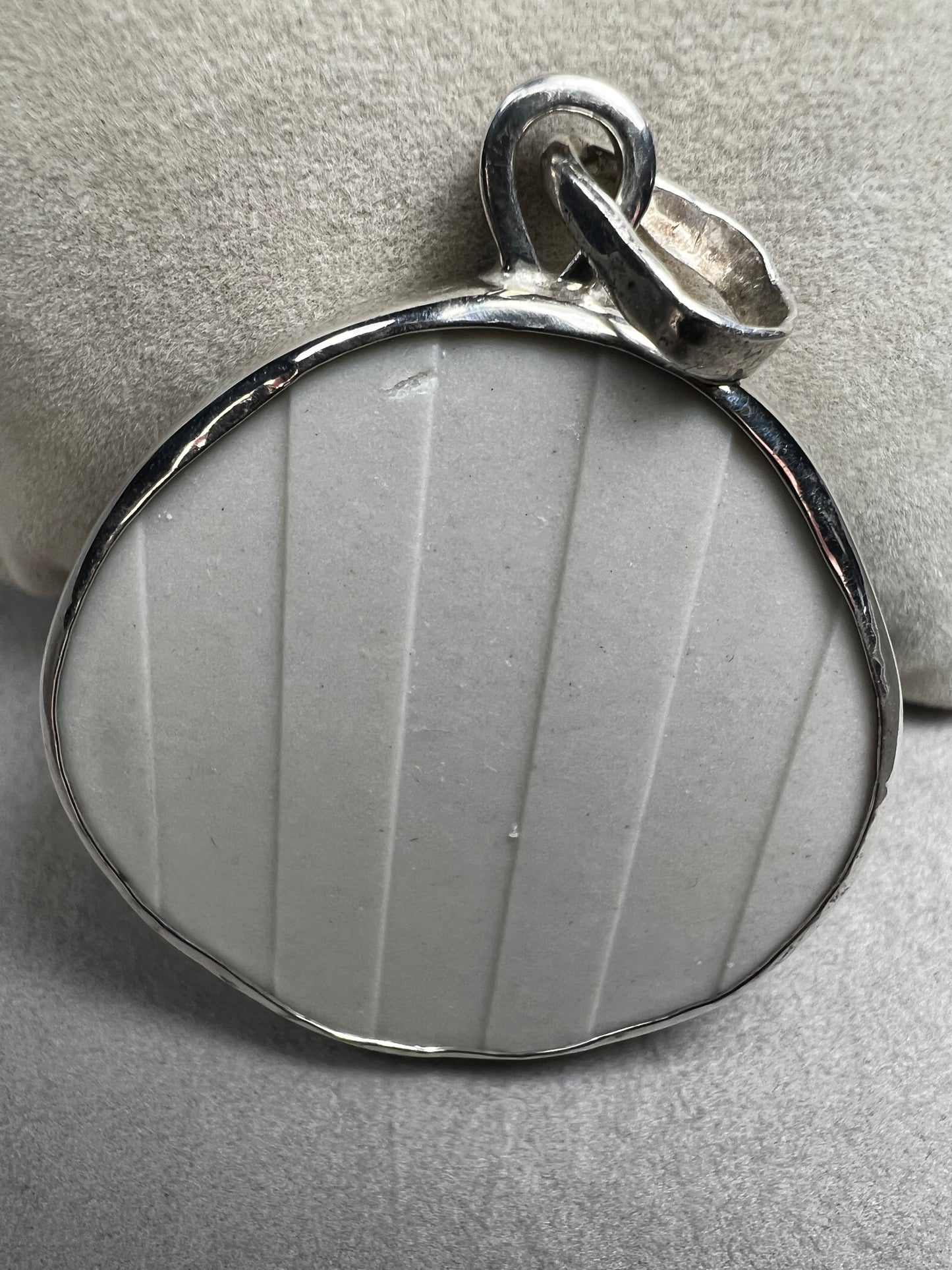 This pendant features a 1.5-inch ceramic disk decorated with a blue and white floral design, framed in sterling silver. Its solid construction makes it a striking piece to wear on a sturdy chain.