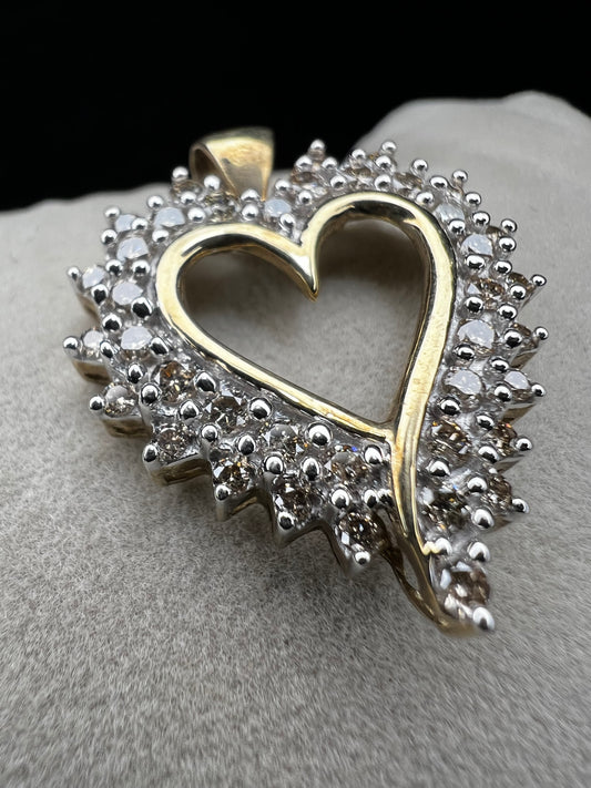 This heart-shaped pendant is crafted with 10 karat yellow gold with a bright white finish around the top to accentuate dazzling natural diamonds that cover the face of this piece.